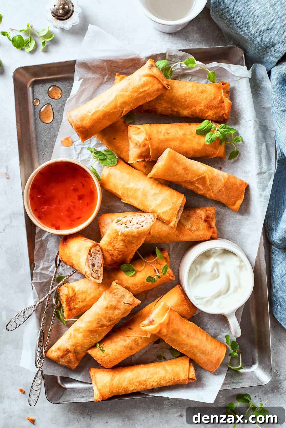 A bowl of red sauce and a bowl of white sauce are served on a serving tray full of chicken egg rolls.