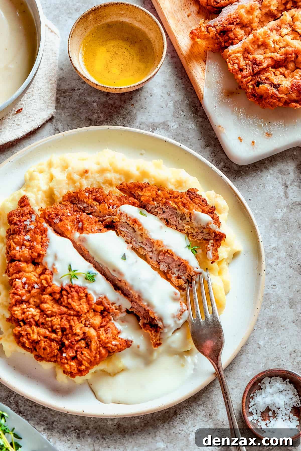 Sliced chicken fried steak served over mashed potatoes, and a fork is resting on top of the meat.