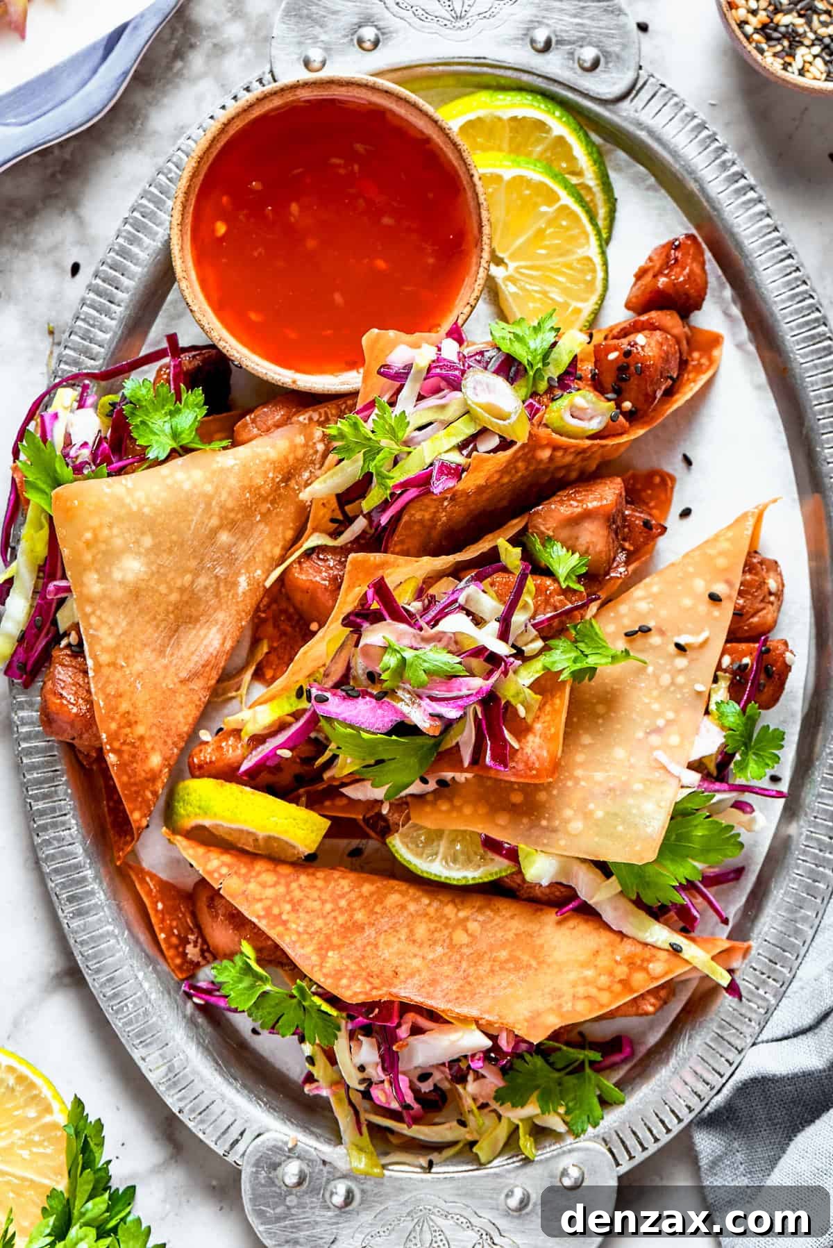 Chicken wonton tacos arranged on an oval platter with a bowl of sauce set right next to the tacos.