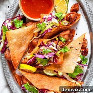 Chicken wonton tacos arranged on an oval platter with a bowl of sauce set right next to the tacos.