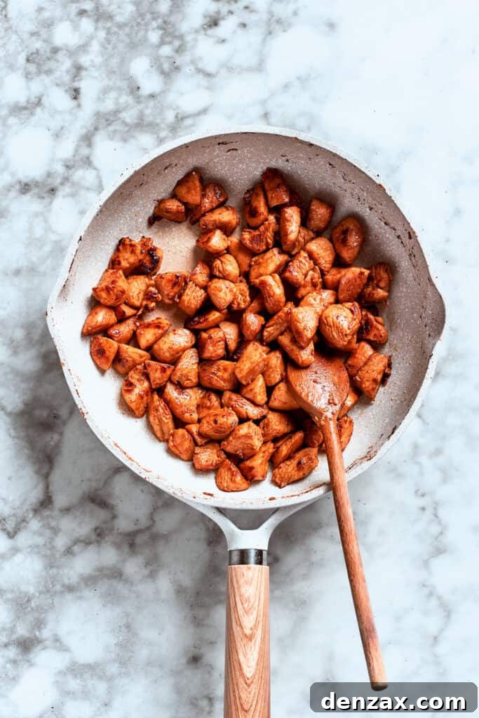 A spoon stirs the chicken as it browns and cooks in the skillet.