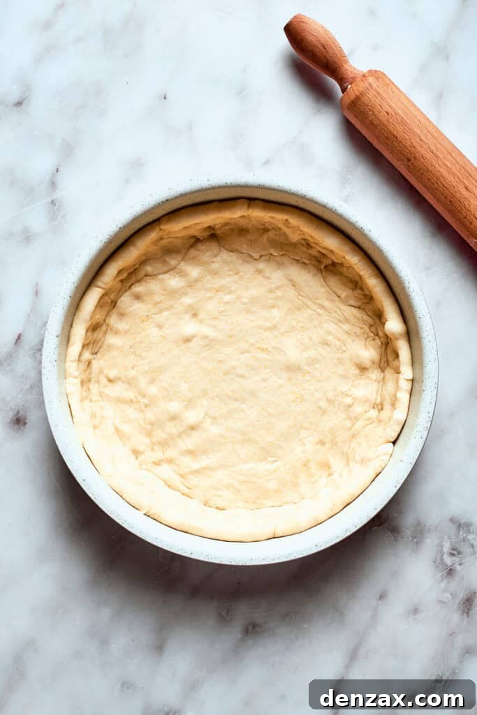 The pizza dough is fitted into a deep sided baking pan.