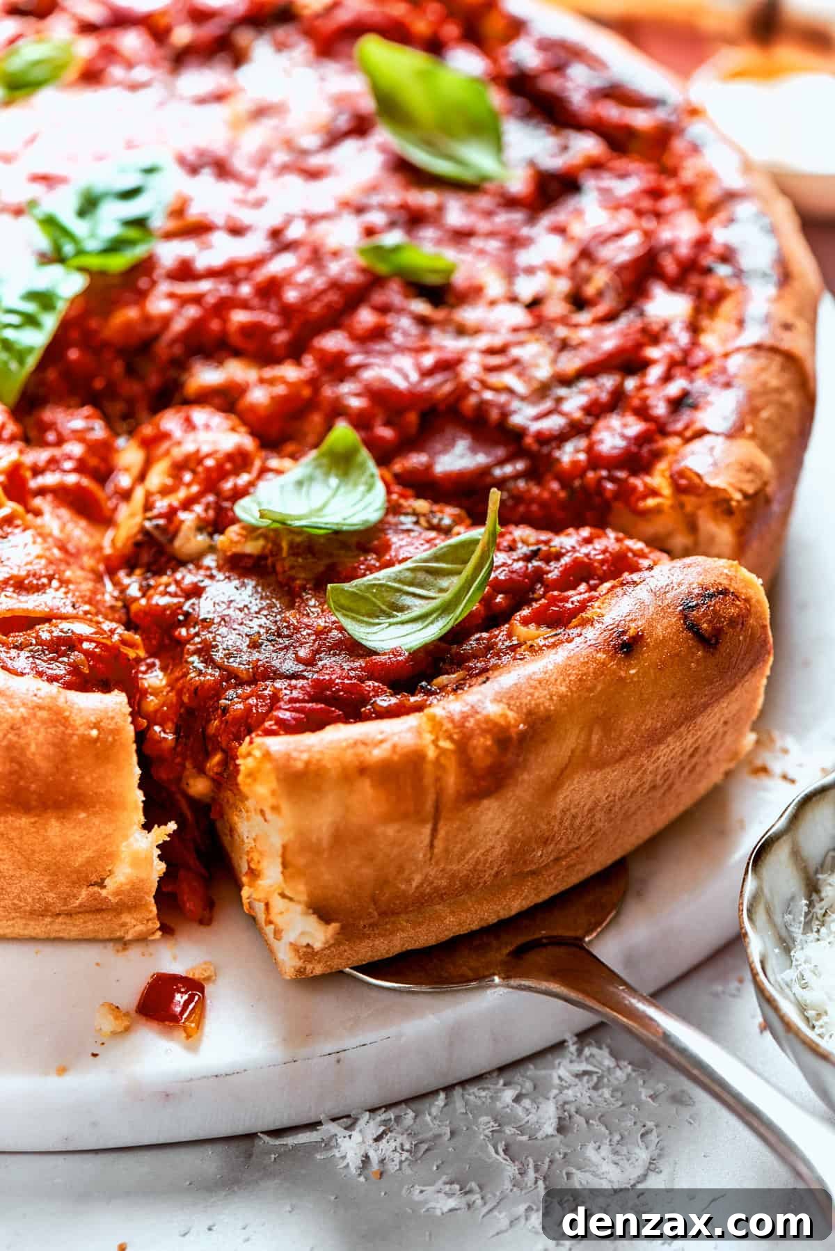 Serving spoon lifting out a slice of deep dish pizza.