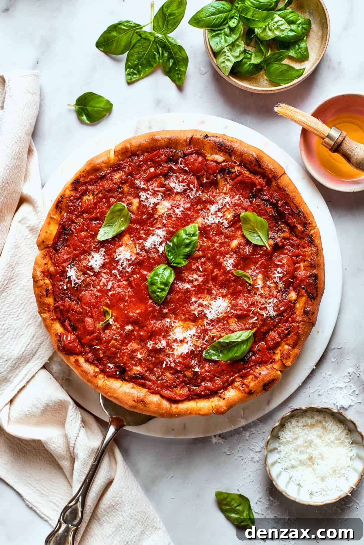 Overhead image of pizza topped with tomato sauce and garnished with fresh basil leaves.