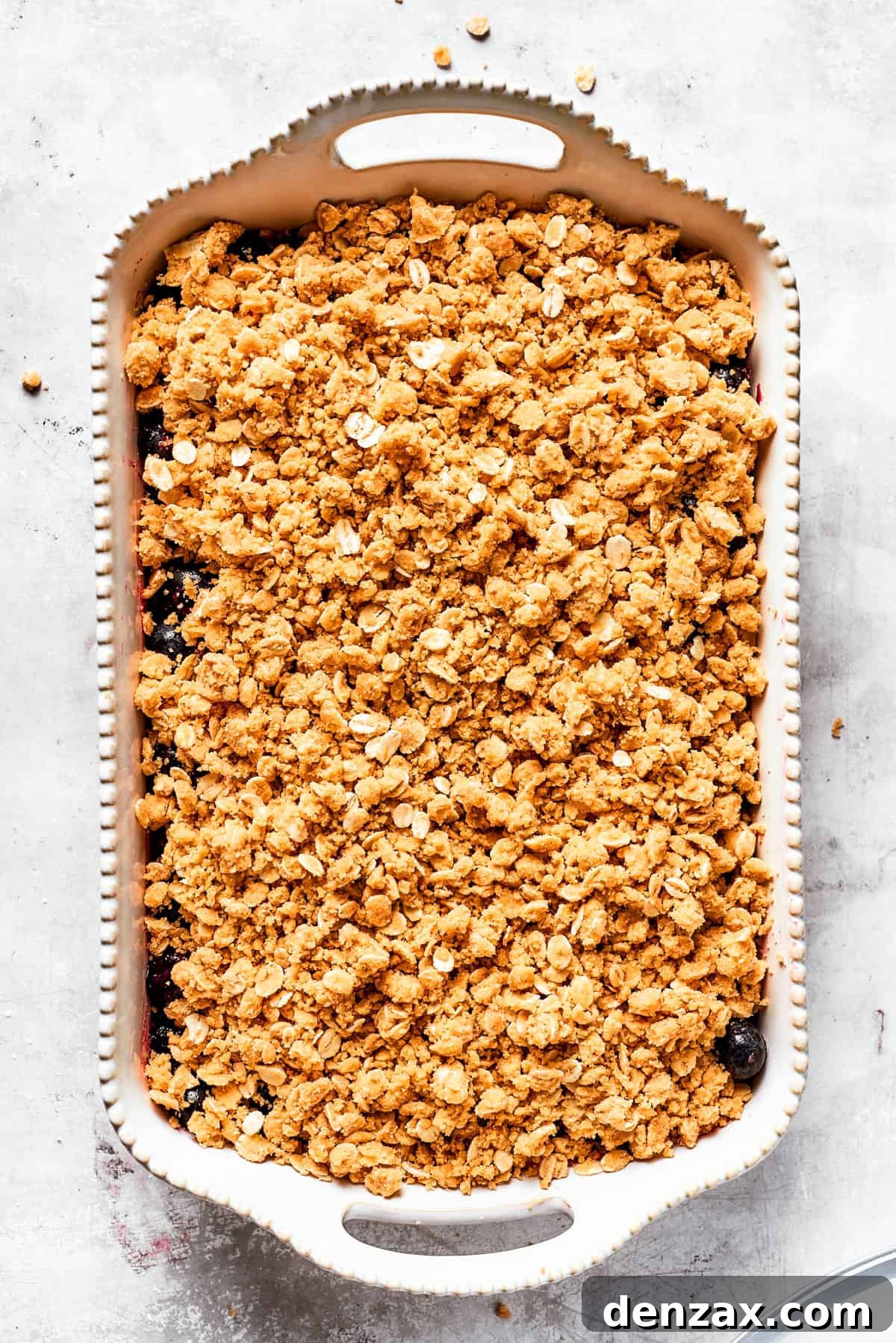 Bursting with juicy berries, this Blueberry Crisp Recipe is topped with a buttery brown sugar and oat crumble. Buttery oats in a baking dish.