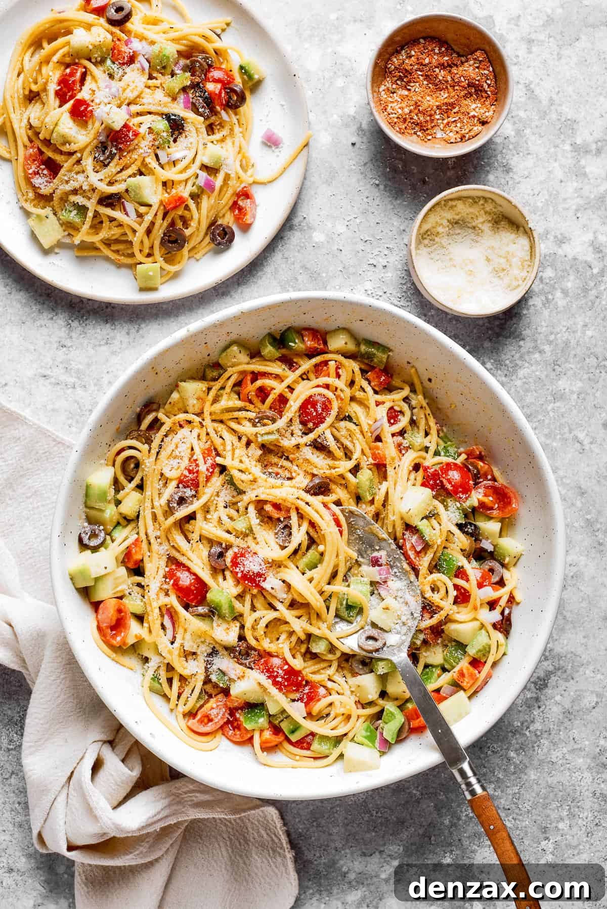 A big bowl of spaghetti salad in a serving bowl with a portion on a plate next to it.