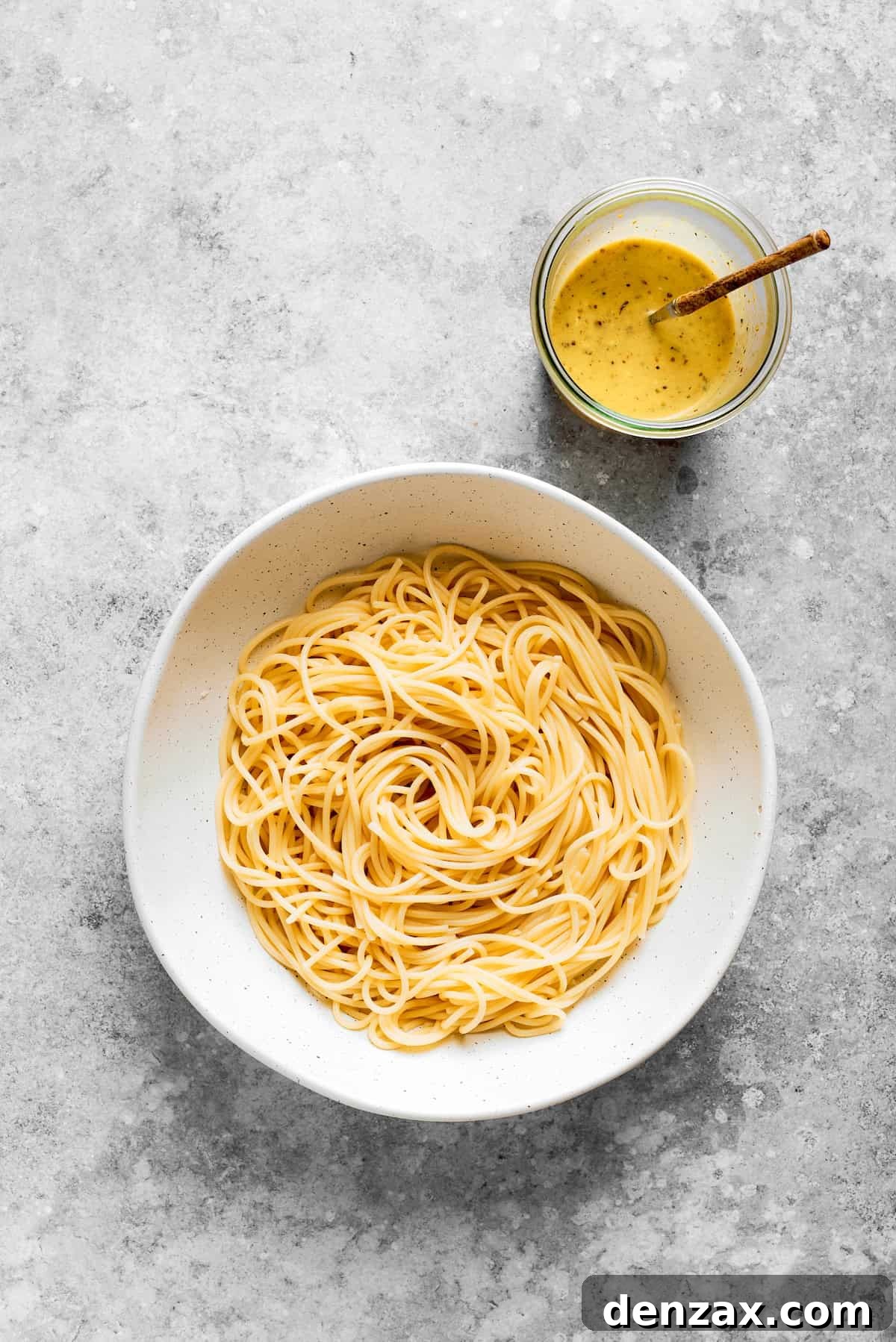 The spaghetti is placed in a bowl with the dressing next to it.