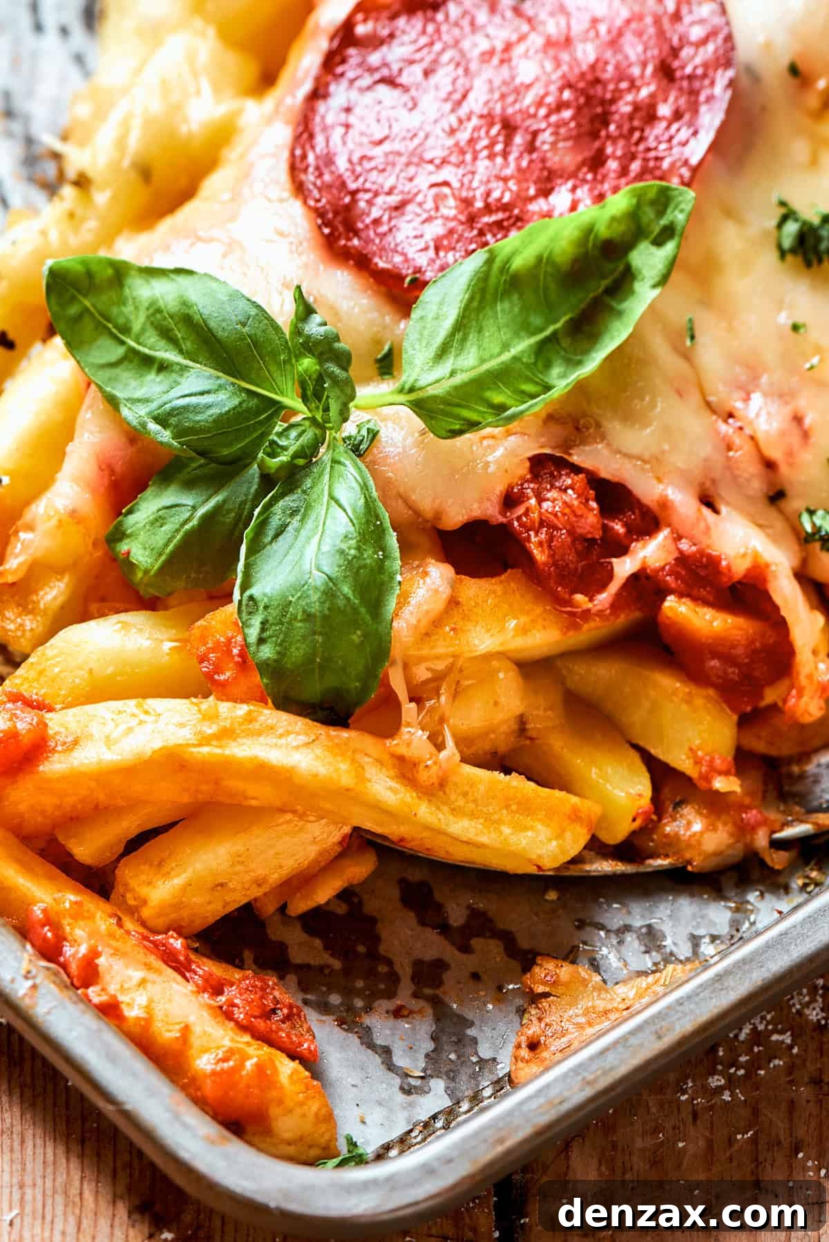 Close-up image of baked french fries garnished with fresh basil leaves.