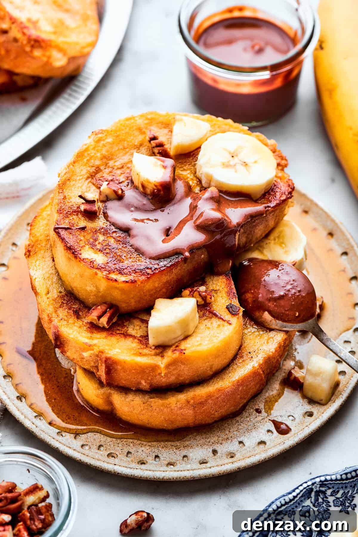 Three slices of French toast stacked on a plate topped with banana slices and Nutella.