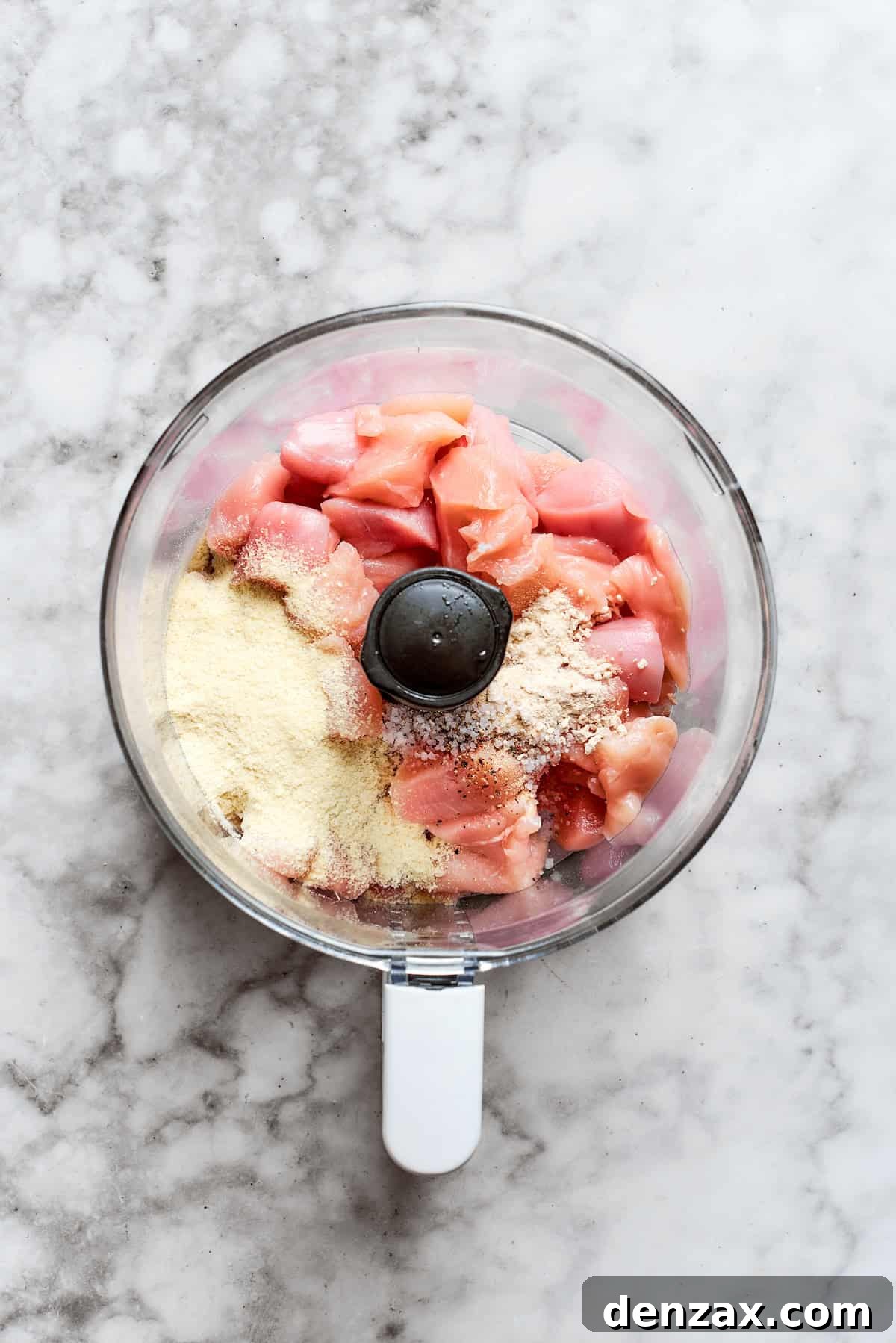 Chicken pieces and spices are added to a food processor.