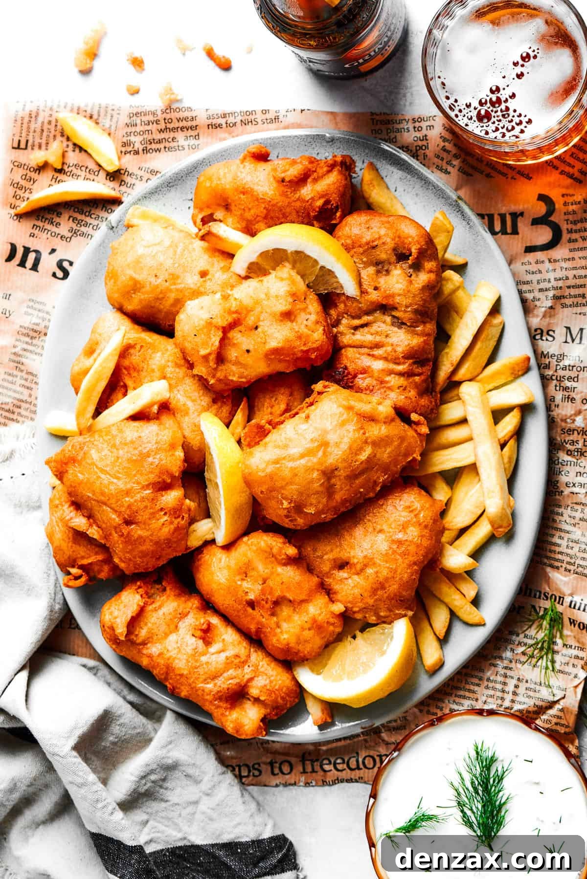 Overhead photo of battered fried shrimp served on a platter with fries, with bottles of beer set next to it and also a bowl of tartar sauce.