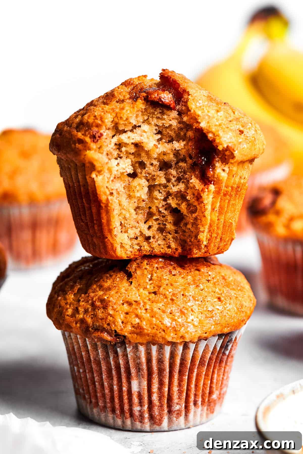 A banana muffin bitten into stands on top of a whole banana muffin.