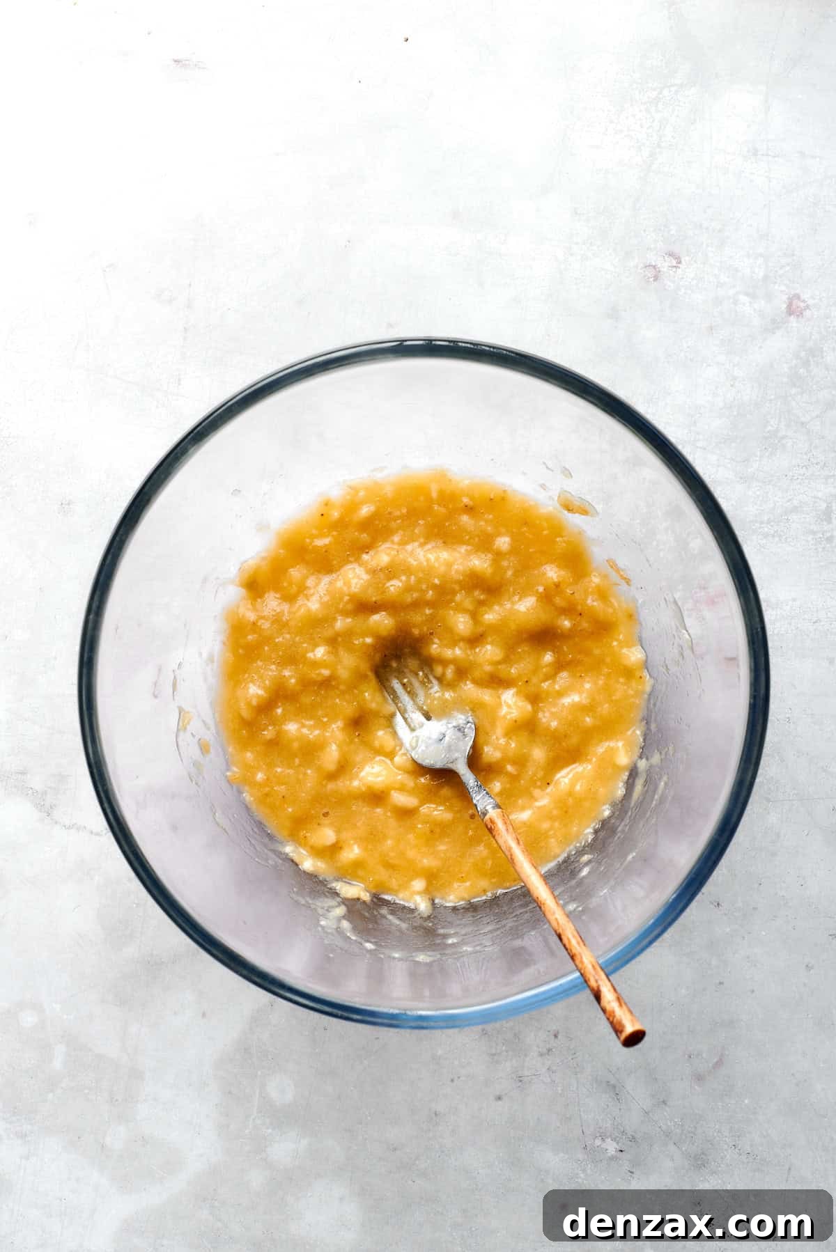 Bananas are mashed with a fork in a bowl.