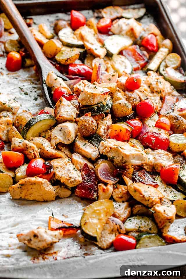 Sheet Pan Chicken with Roasted Vegetables Dinner 4 side view of mixing chicken and vegetables on a baking sheet with a brown wooden spoon