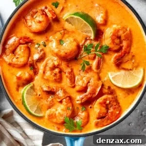 A skillet of cooked shrimp in tomato sauce. There are lime wedges arranged all around the shrimp.