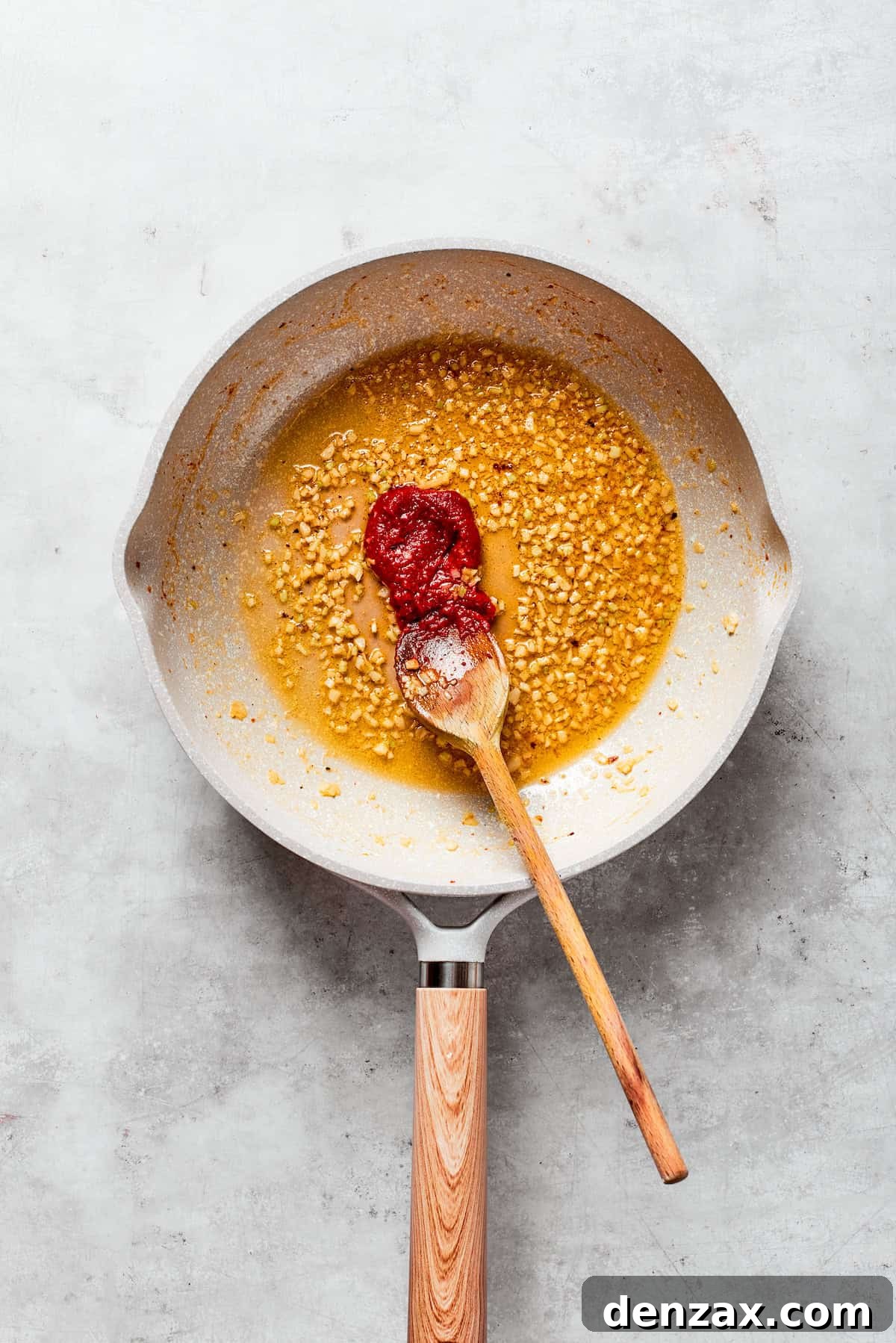Tomato paste is added to a skillet with butter and garlic.