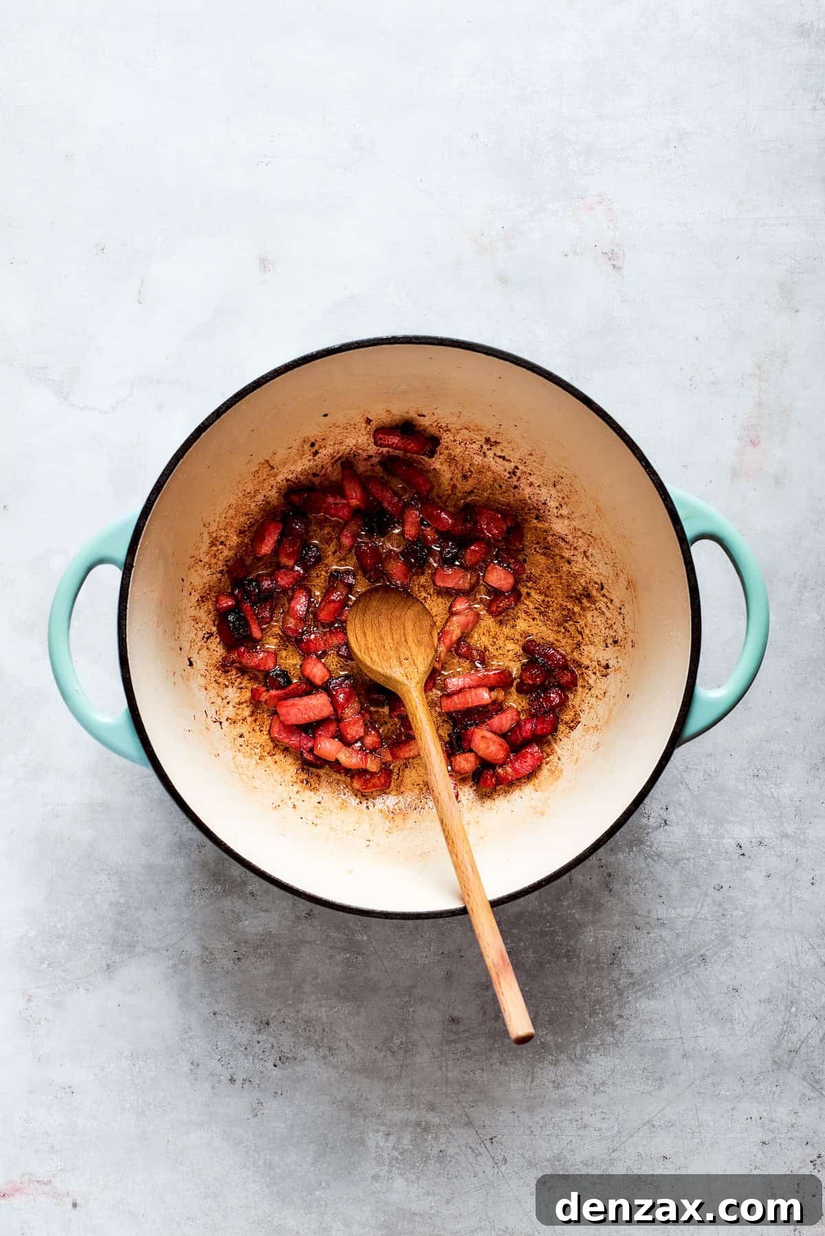 A spoon stirs chopped bacon in a pot.