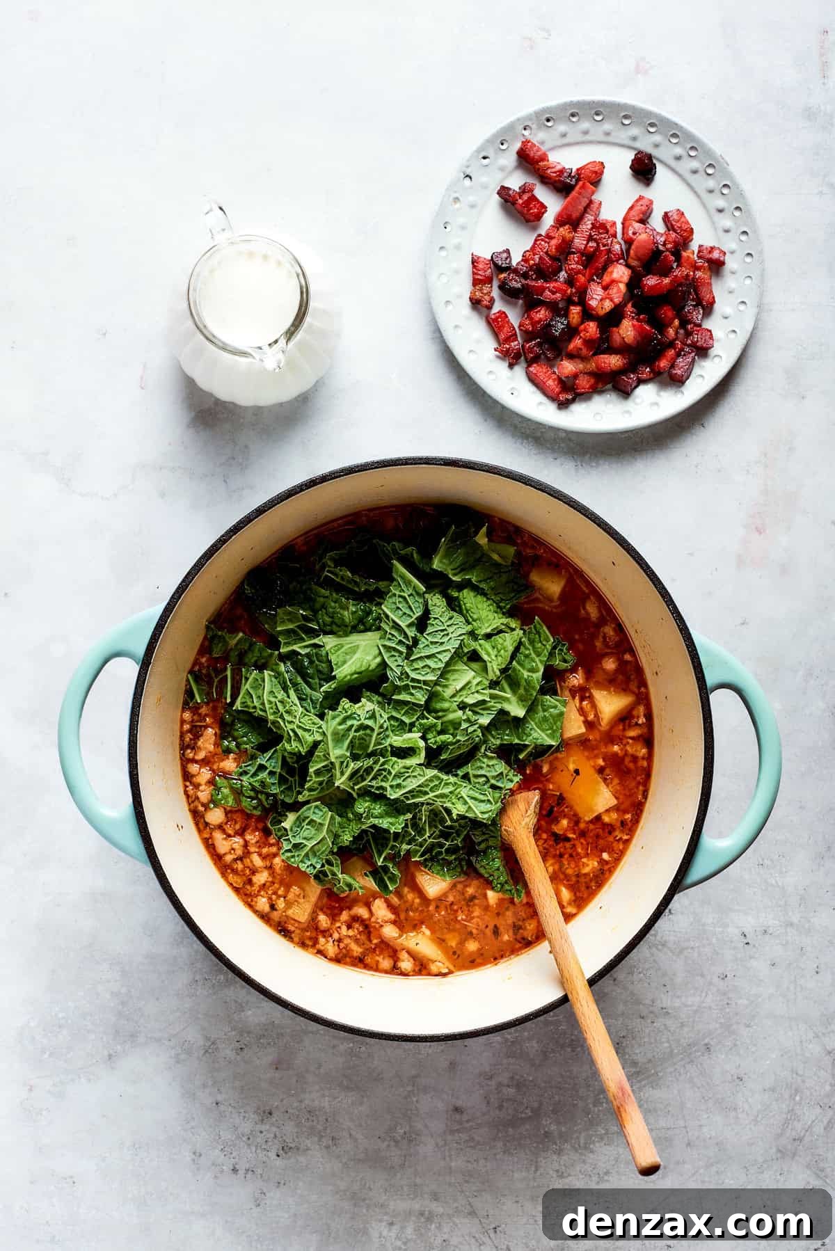 Kale is added to the top of the soup pot.