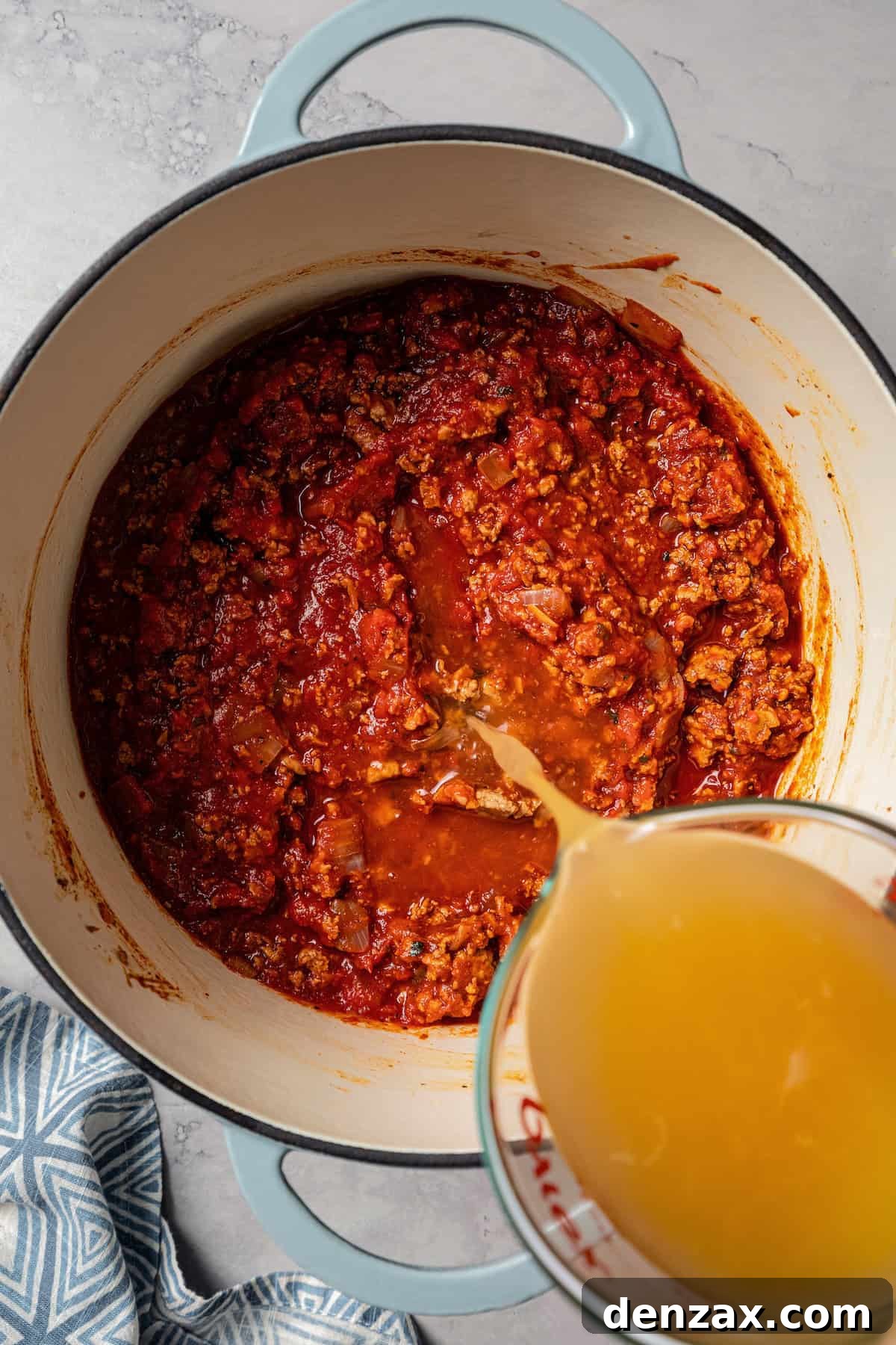 Chicken broth being poured over the other turkey chili ingredients in a pot.