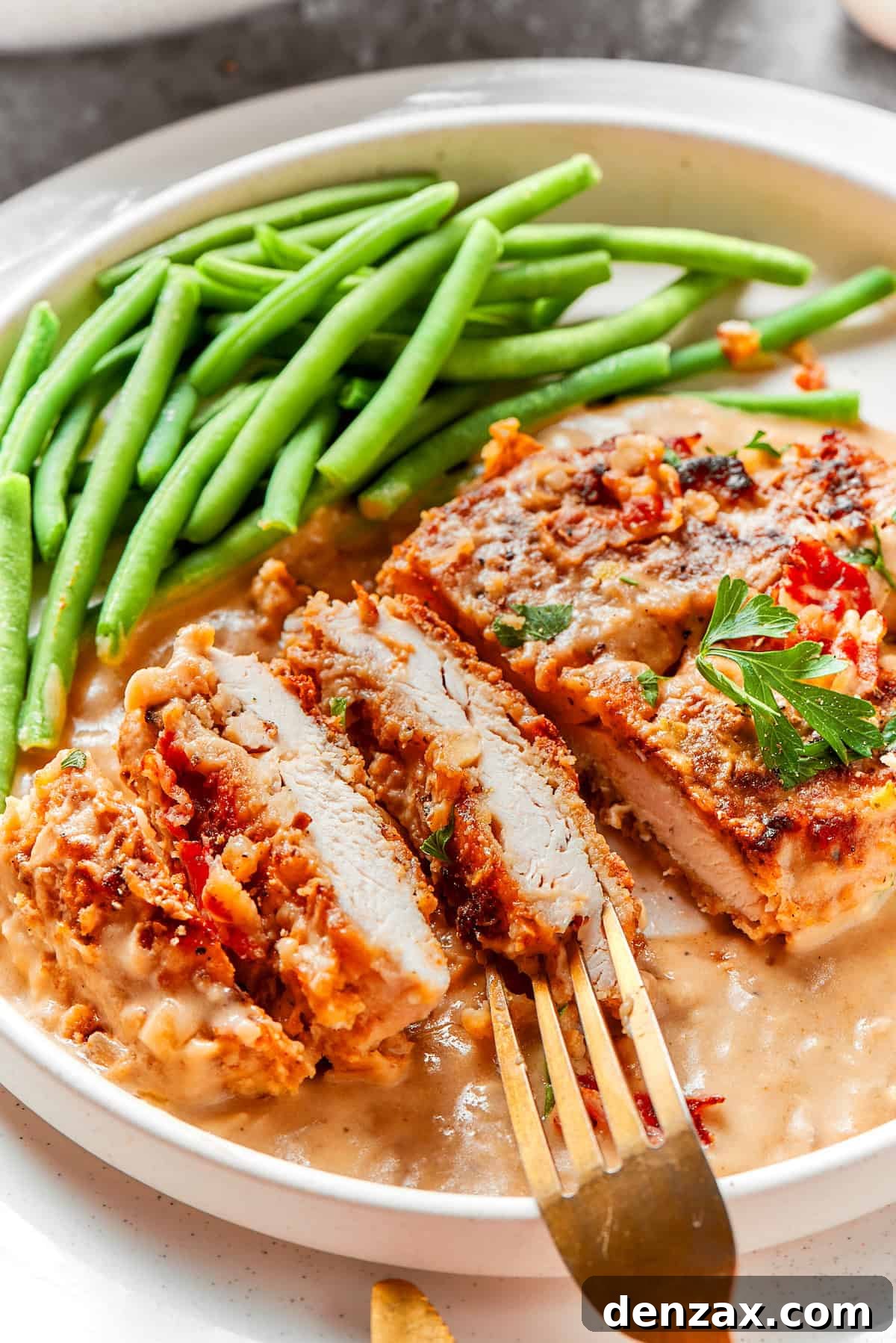 A piece of smothered chicken sliced on a plate with green beans.