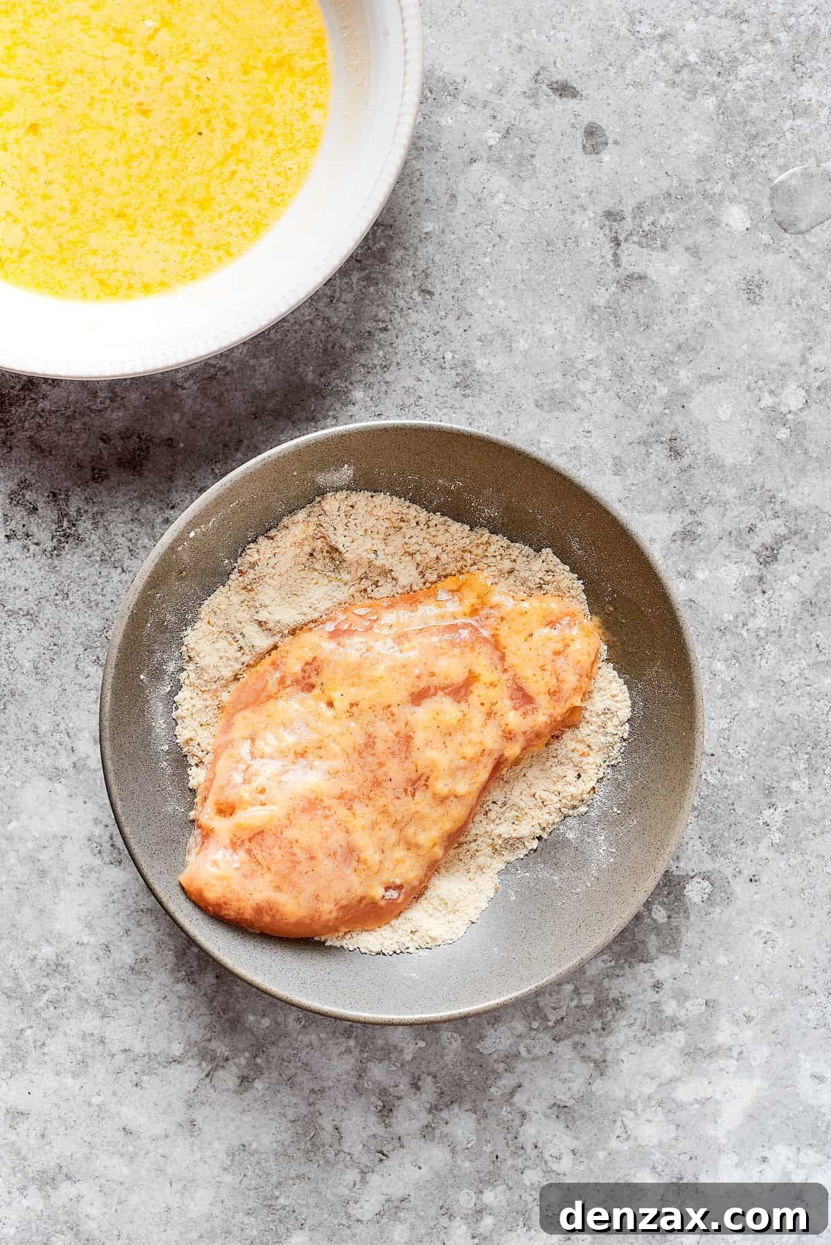 A chicken breast is dredged in breadcrumbs.