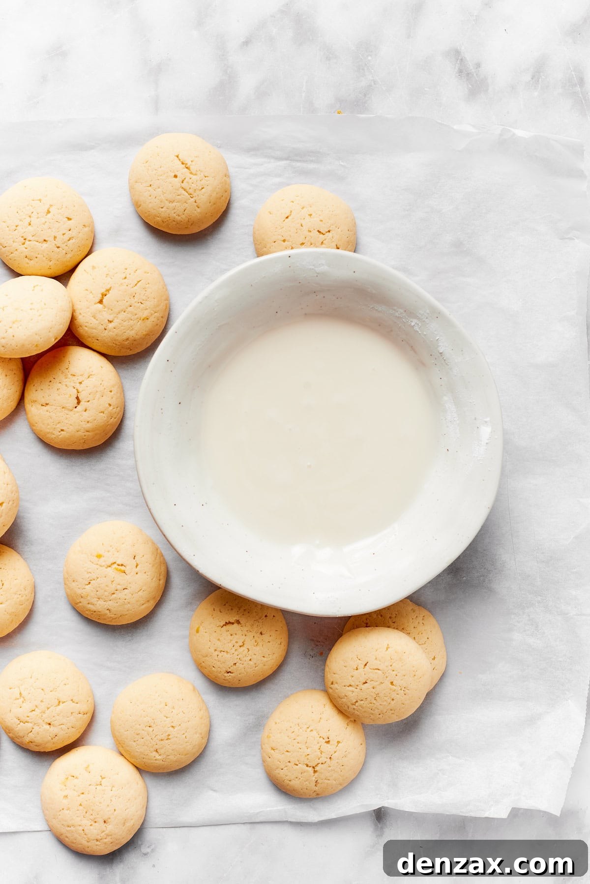 A bowl of icing surrounded by anginetti cookies.