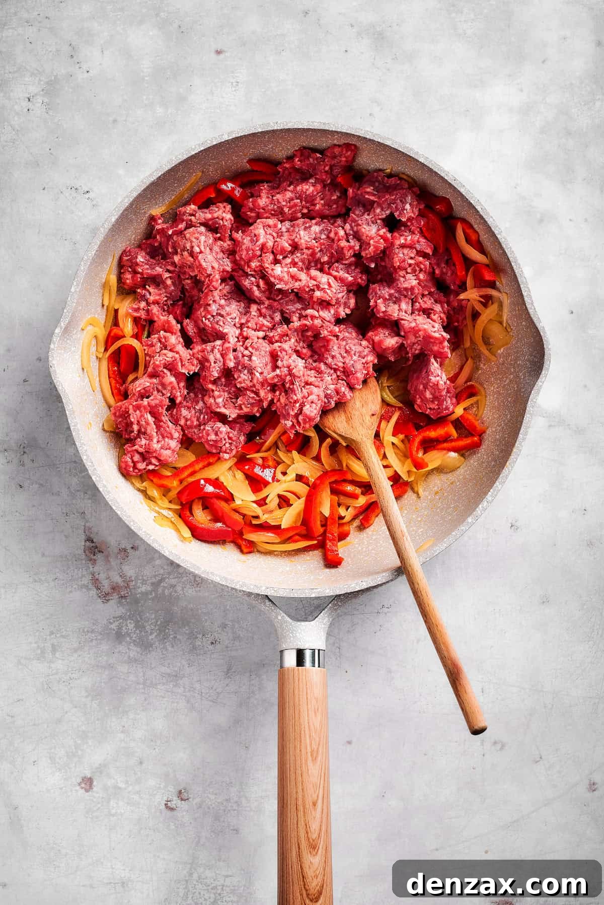 Cook onions and peppers, then add beef. Adding ground beef to onions and peppers in a skillet.
