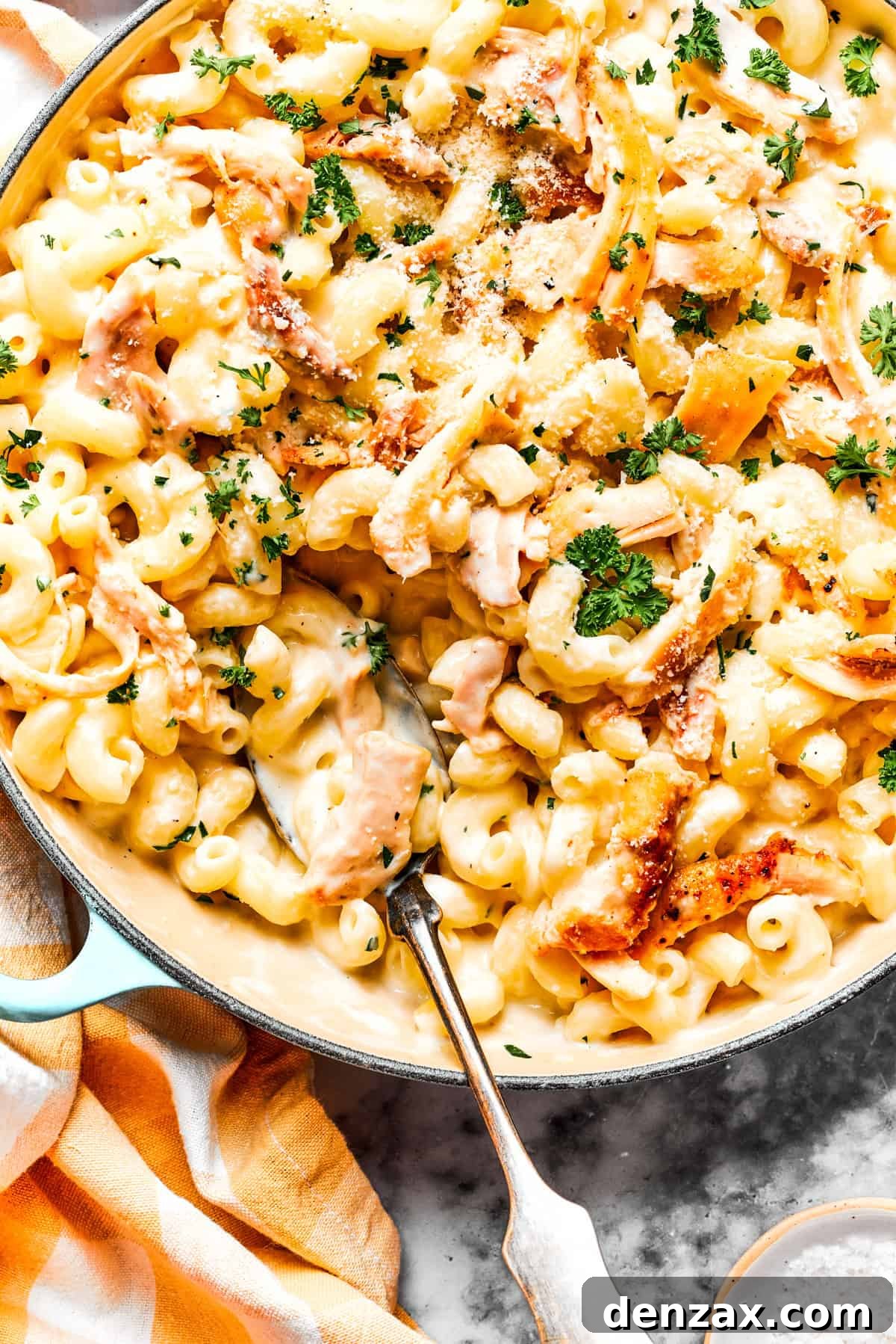 Close-up image of parmesan chicken pasta in a skillet, with a serving spoon resting inside the skillet.