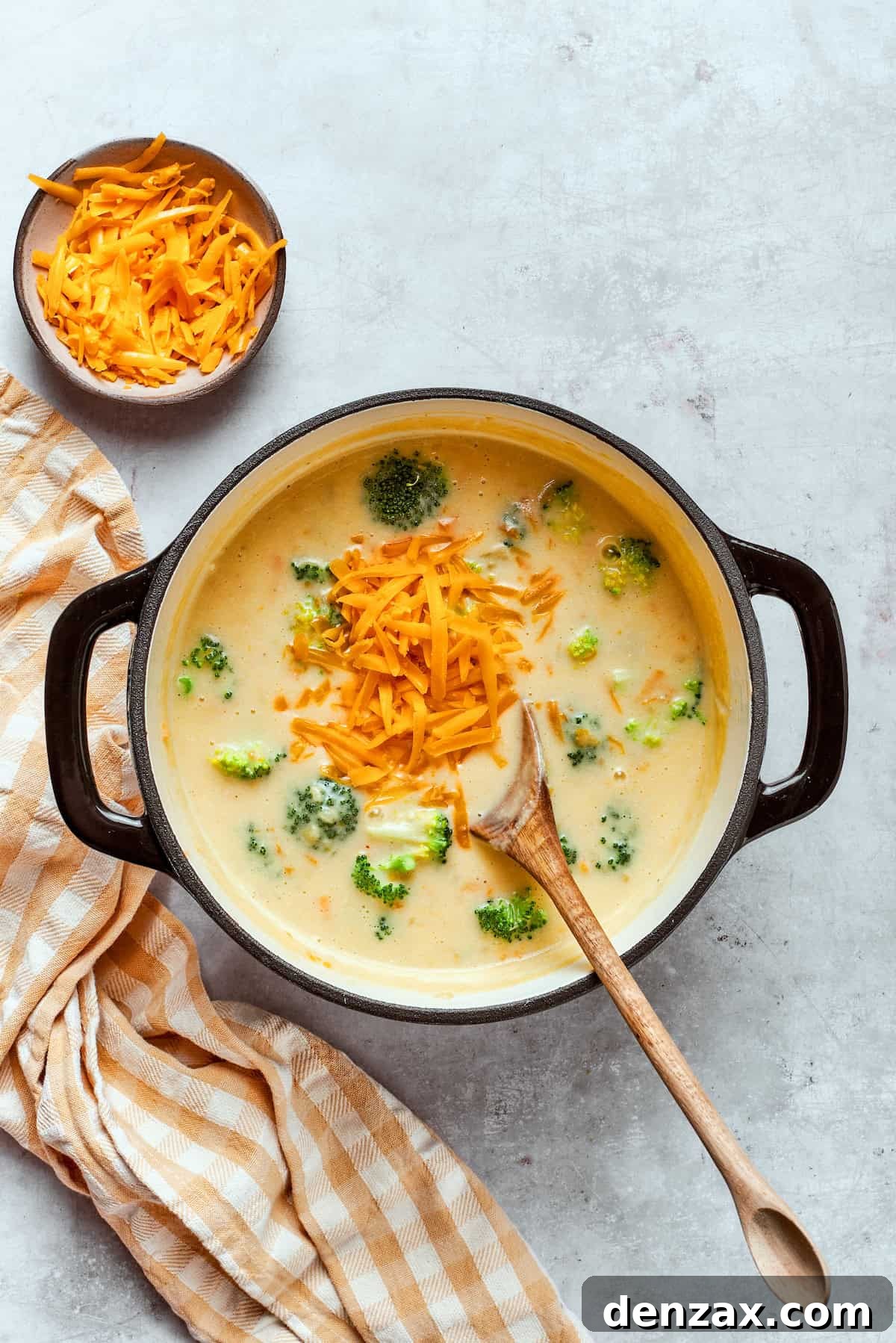 Adding shredded cheddar to a pot with soup.