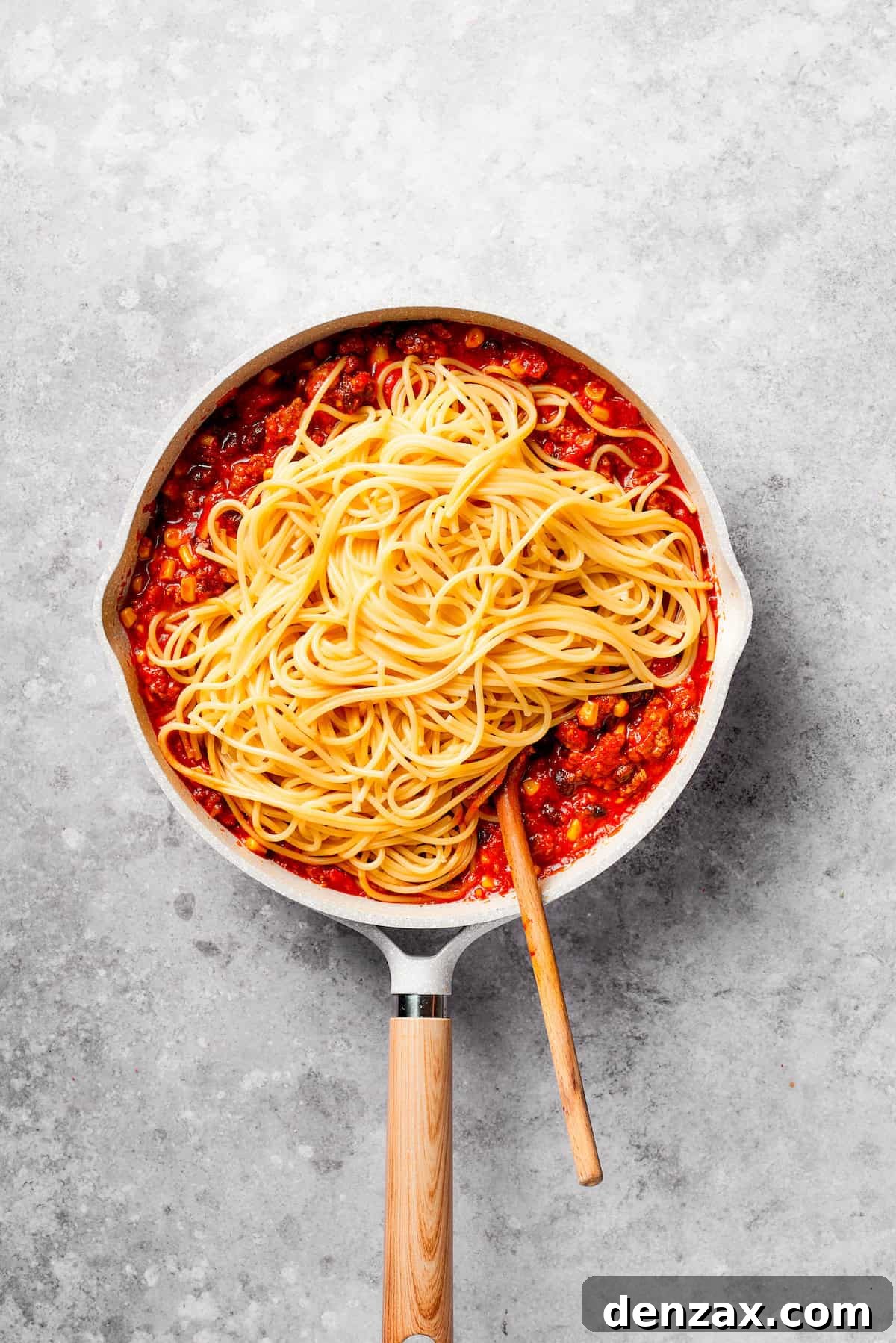 Cooked spaghetti is mixed into other ingredients for Mexican spaghetti.