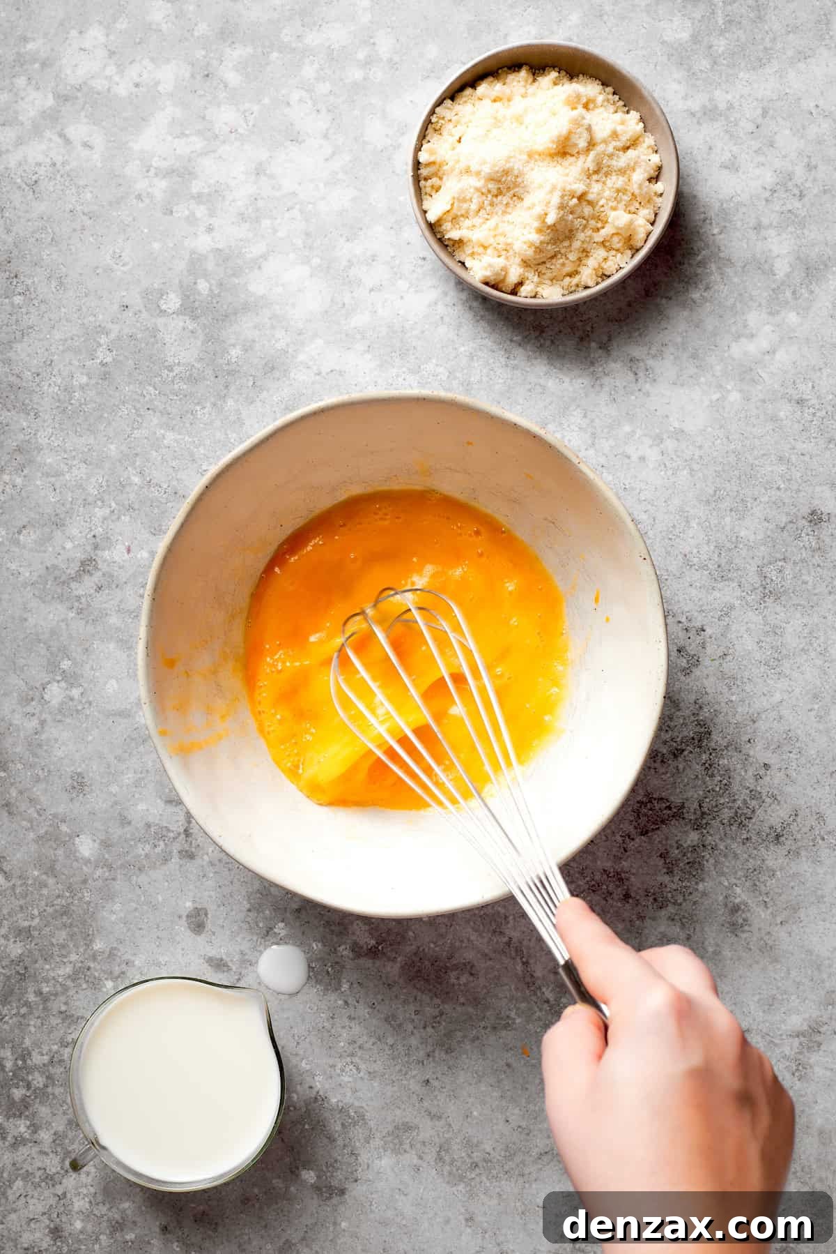A hand uses a whisk to mix eggs.