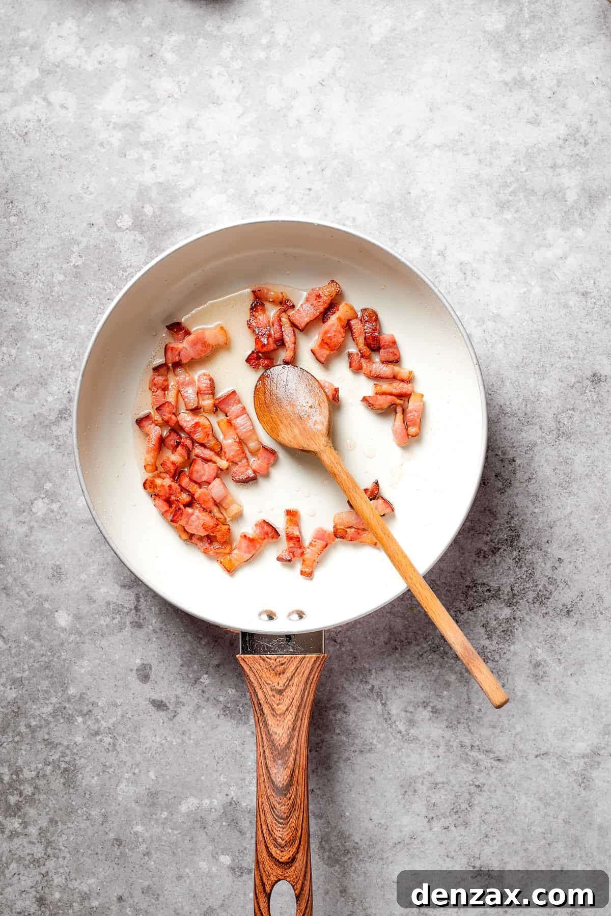 A spoon stirs a skillet of bacon.