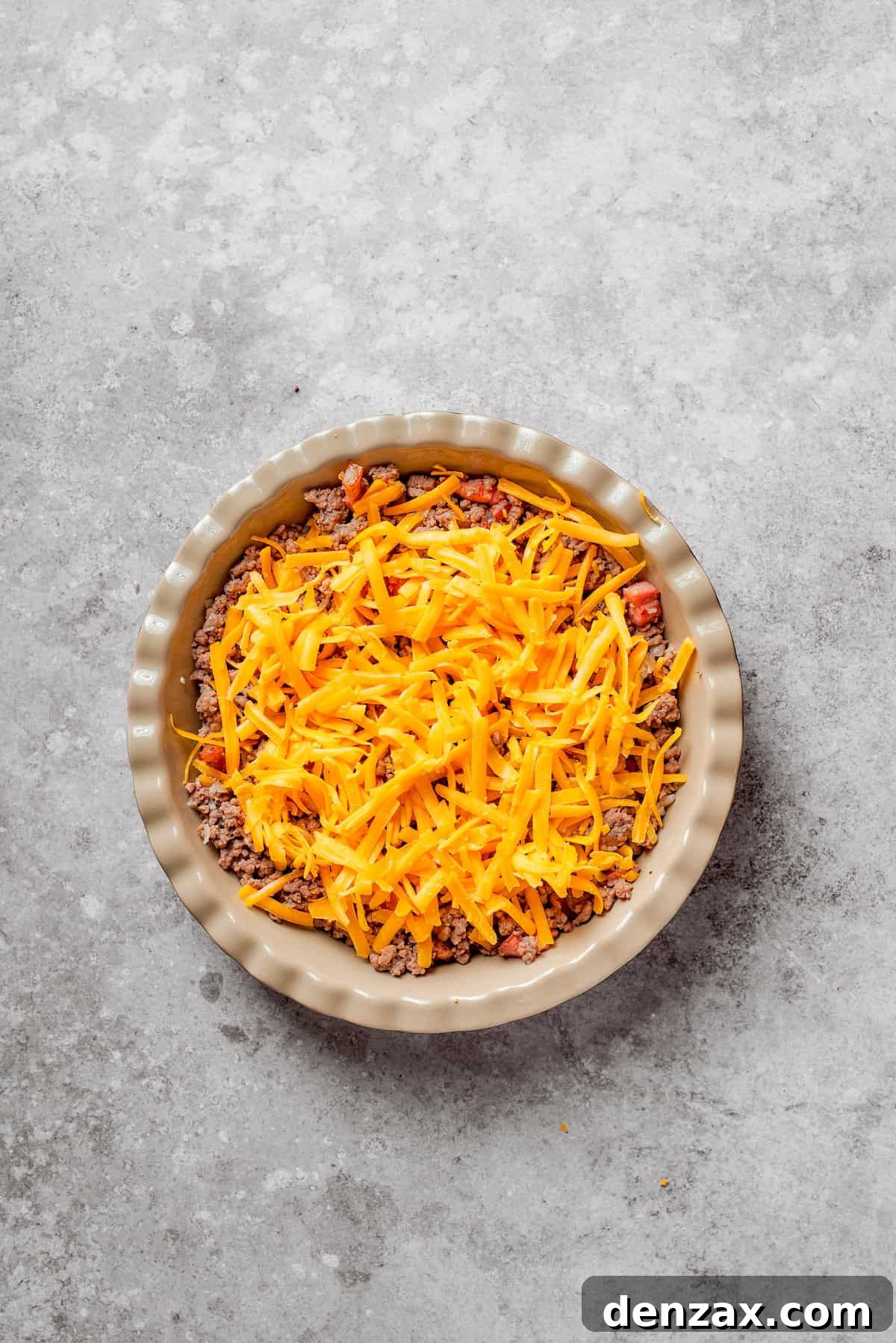 Shredded cheese added to cheeseburger pie.