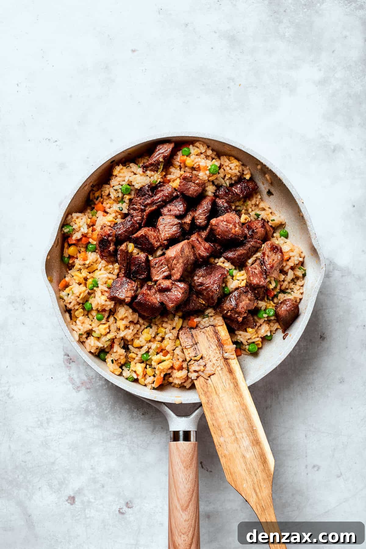 Steak is added to a pan of fried rice.