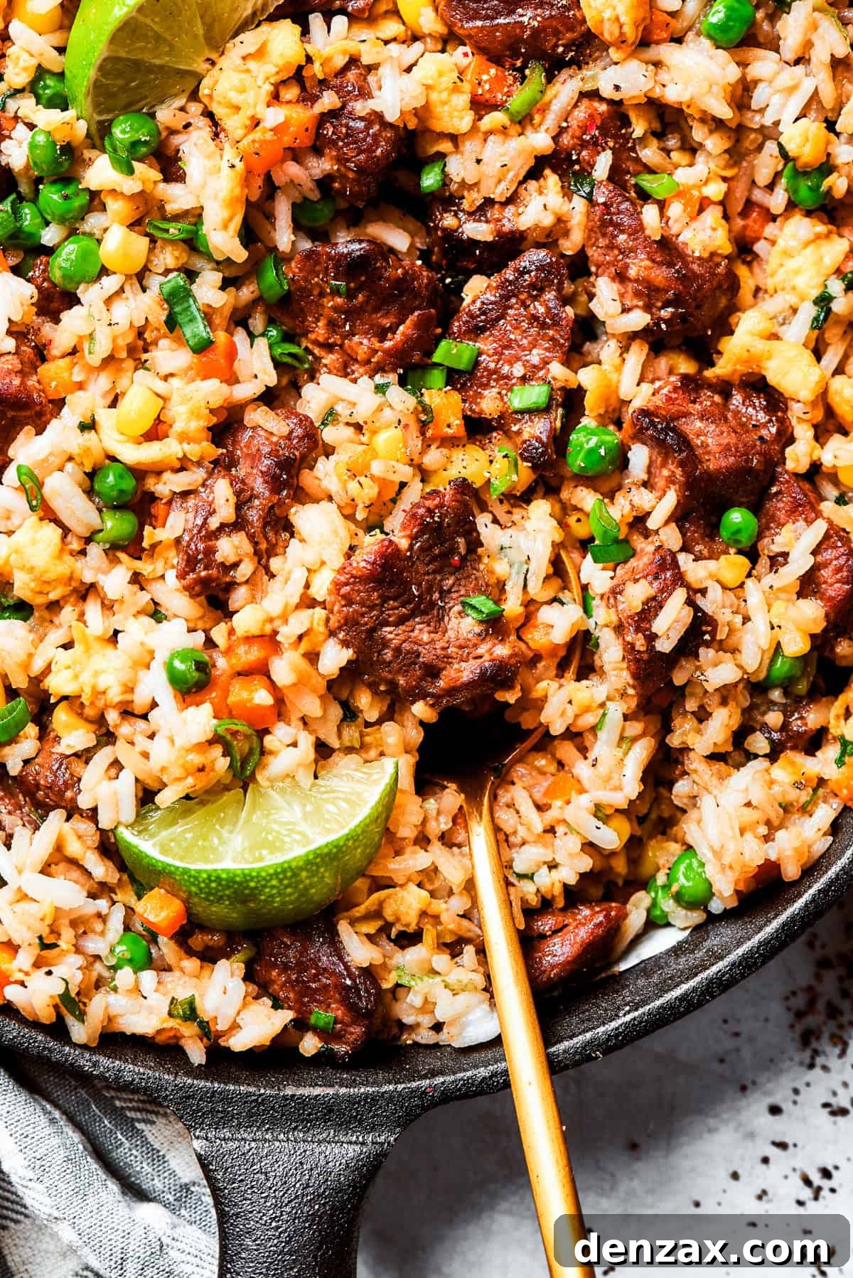 Stirring through steak fried rice garnished with lime wedges and green onions.