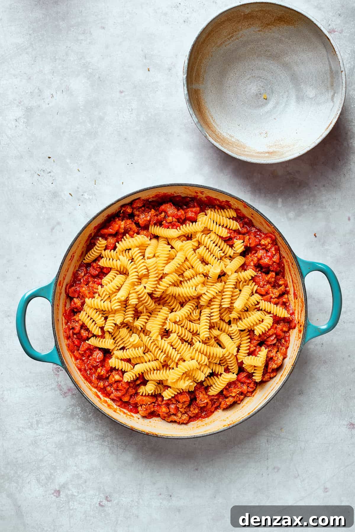 Pasta is added to a pan of sauce.