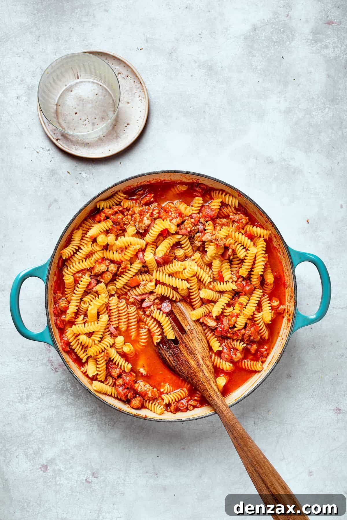 A spoon stirs the pasta into the sauce.