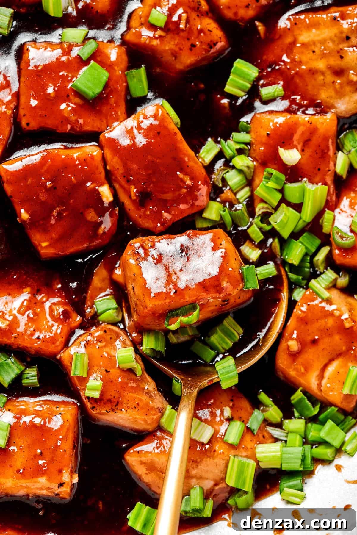 A spoon in a serving of teriyaki salmon.