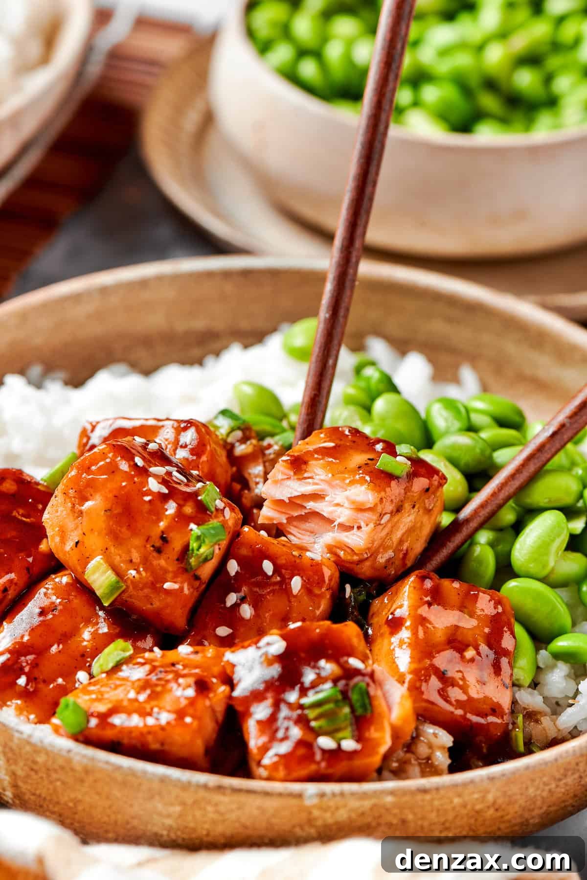 Chopsticks pick up a piece of teriyaki salmon.