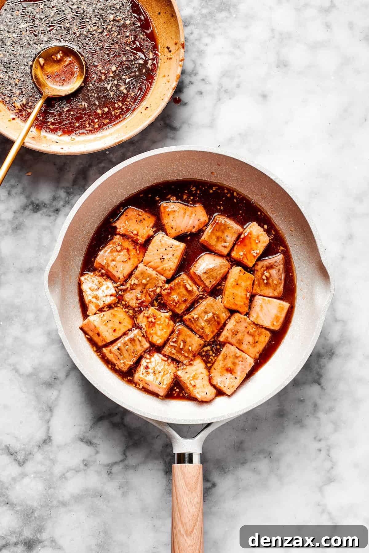 Salmon cooks in a skillet with sauce.
