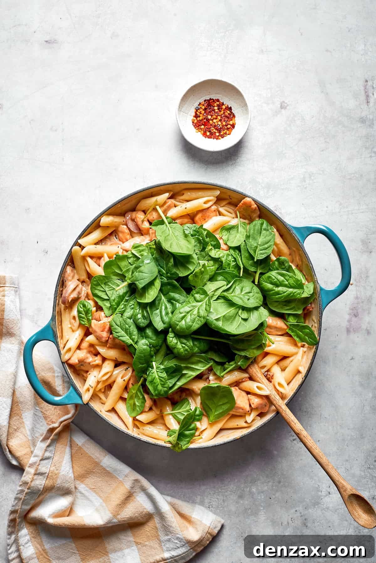 Spinach leaves added to a skillet of marry me chicken pasta.