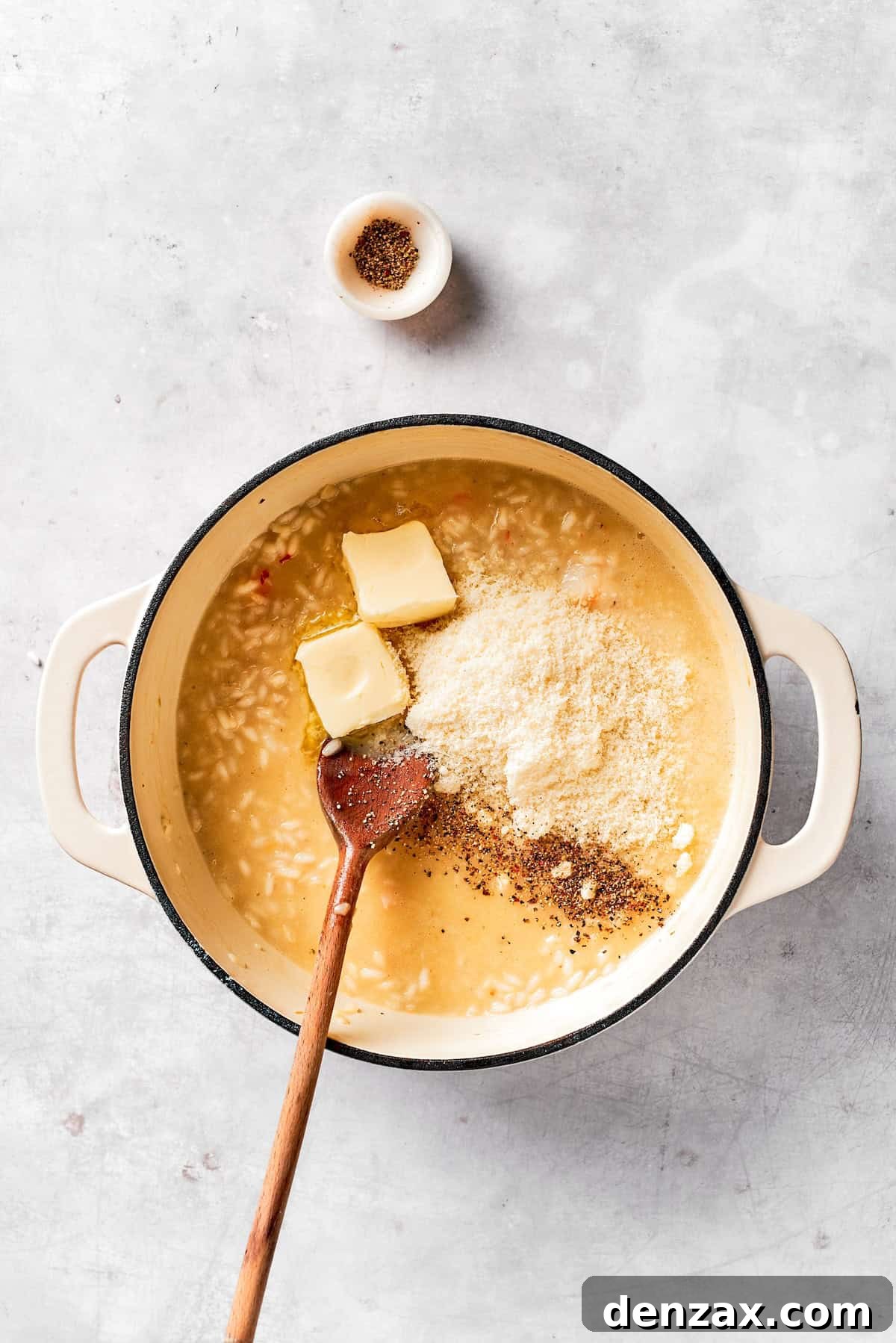 Cheese and butter are added to a pot of risotto.