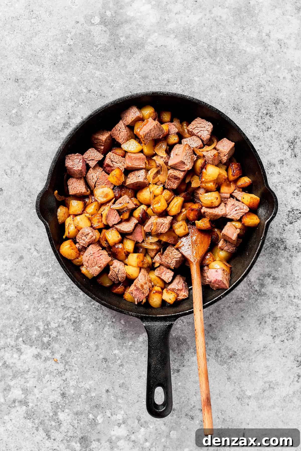 Steak is stirred into a cast iron skillet with potatoes.