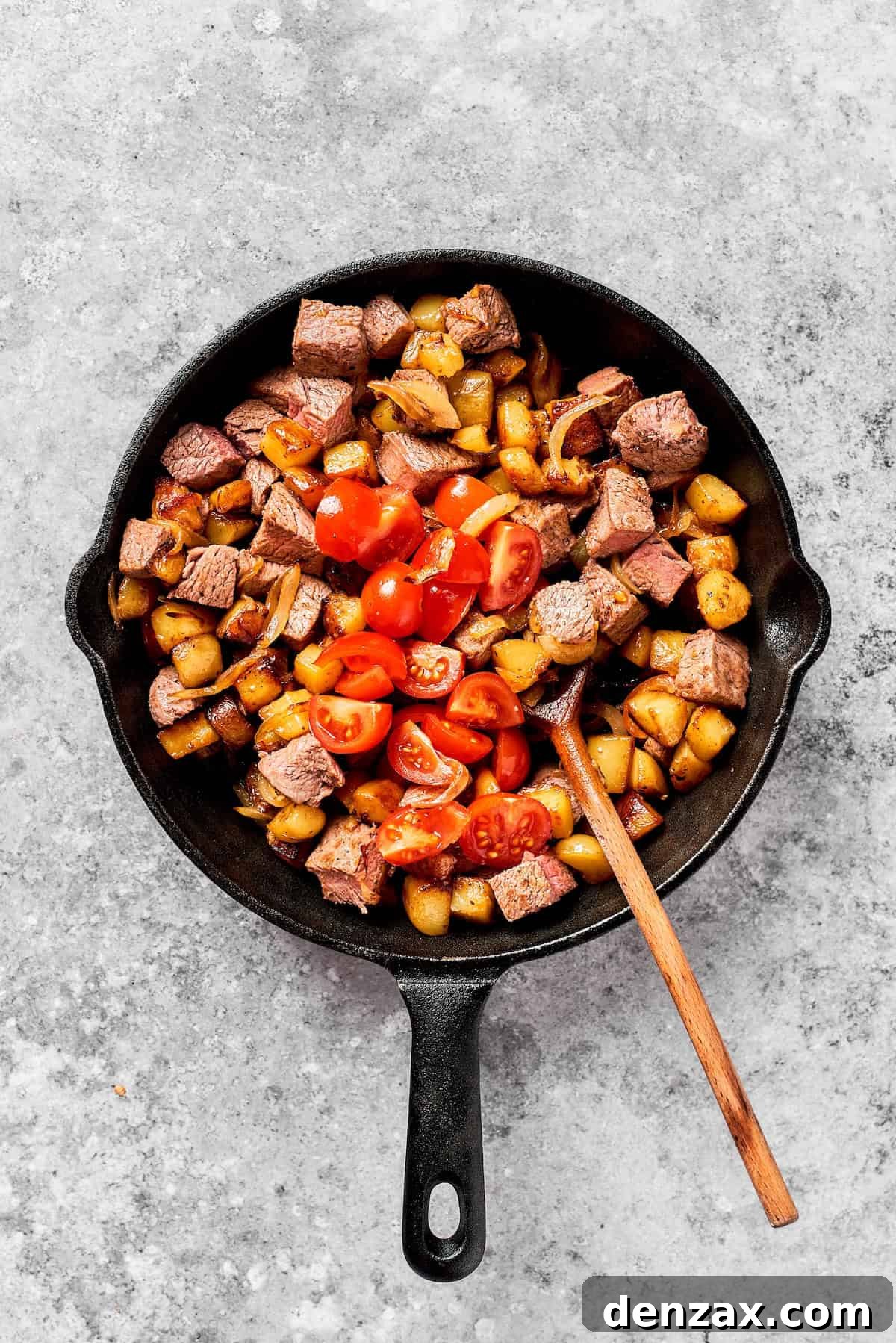 A spoon stirs a skillet of steak and potatoes.