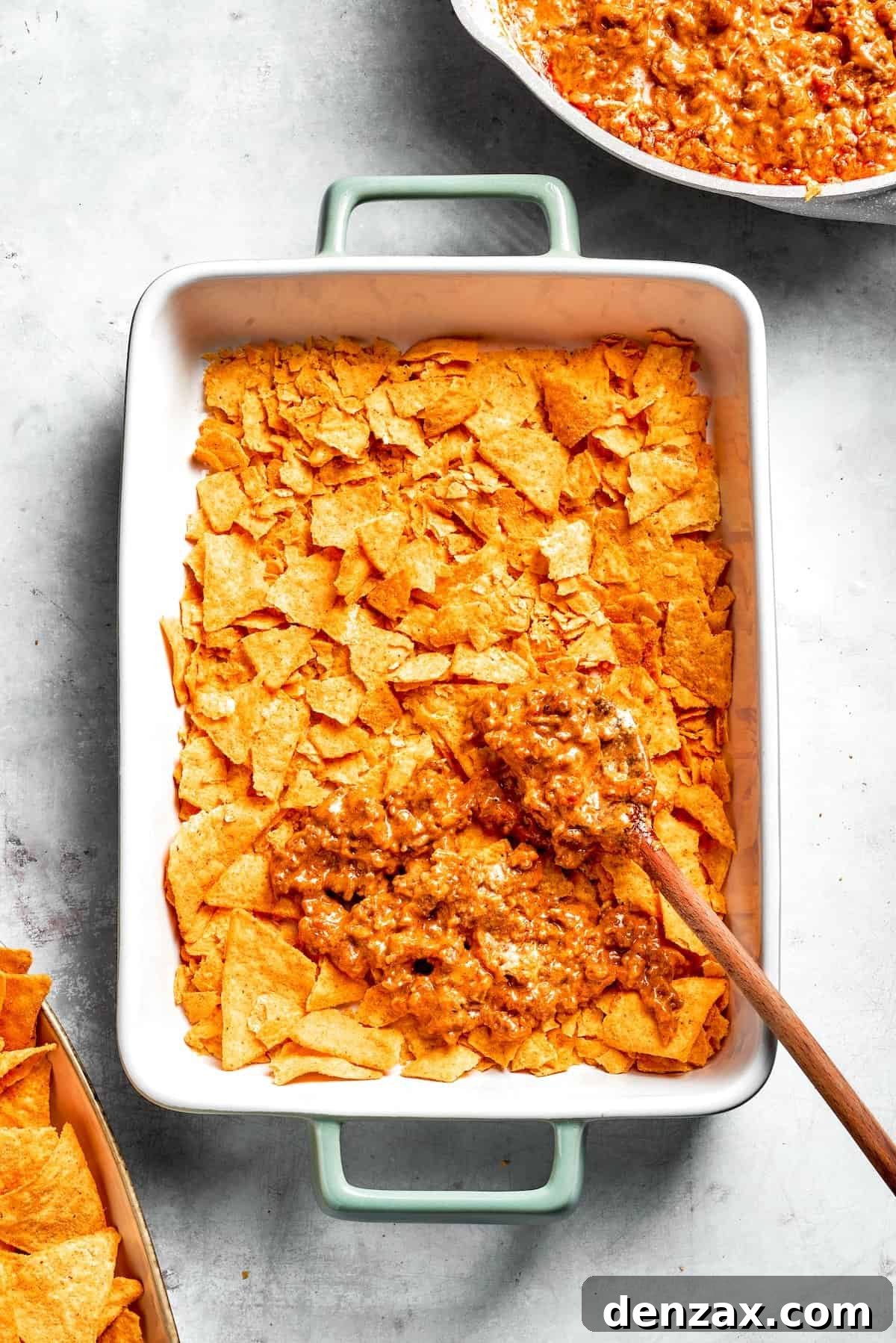 A casserole dish with a layer of Doritos being topped with beef filling.