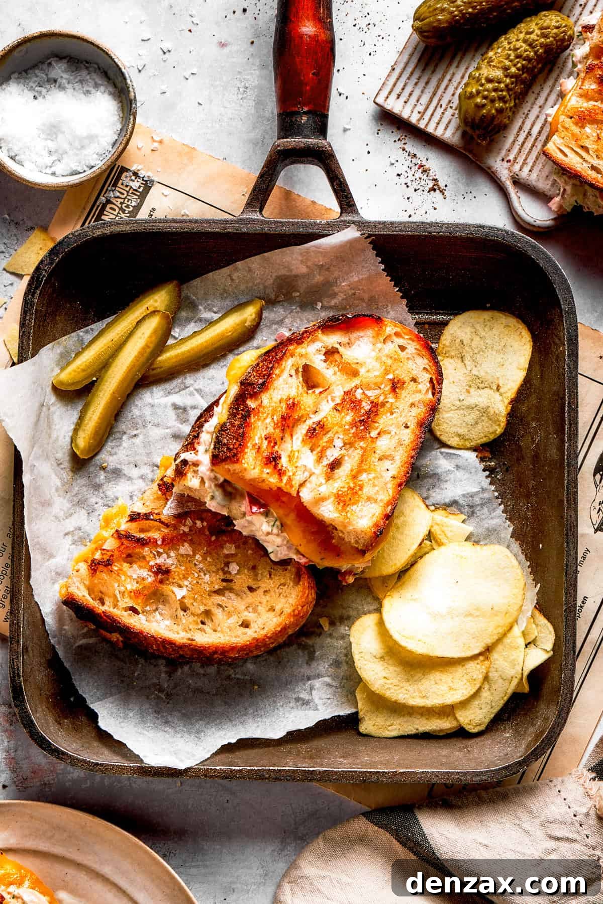 Two tuna melt sandwiches in a skillet with a pile of potato chips arranged next to them.