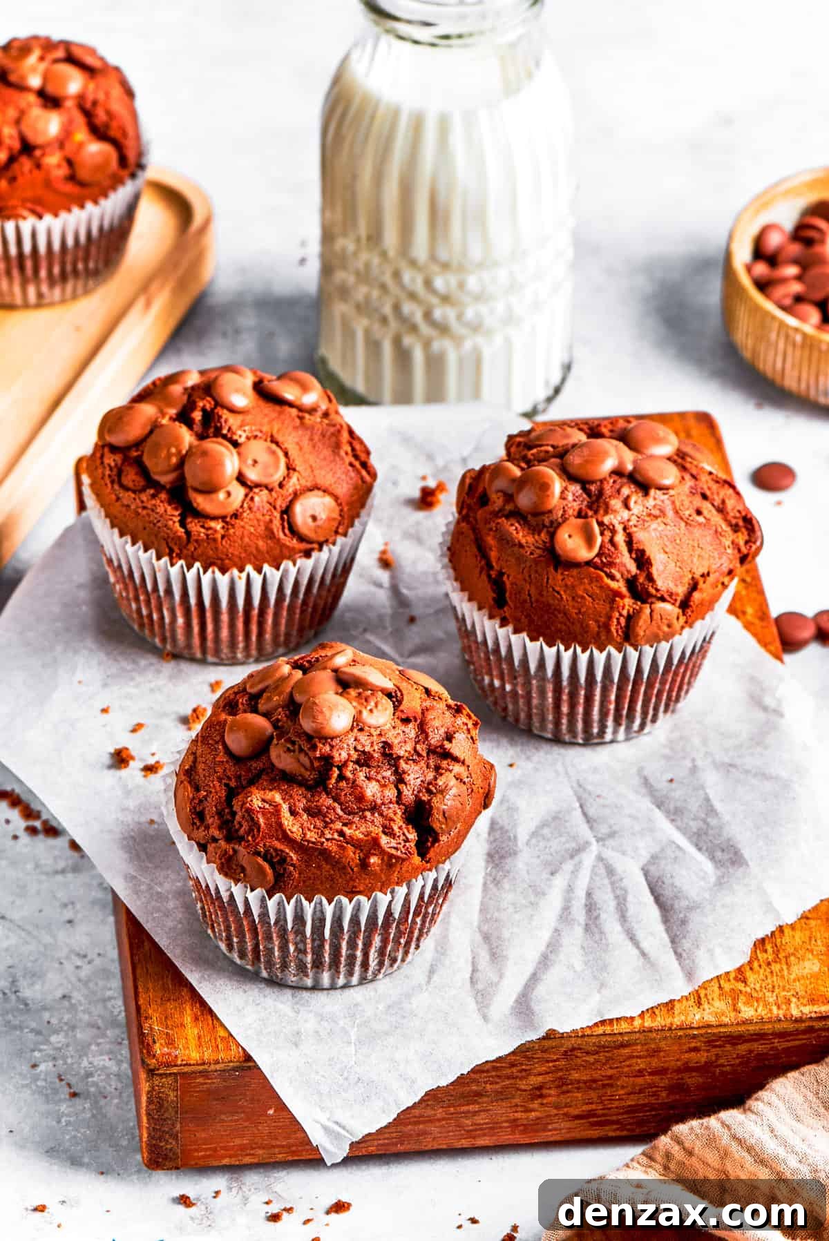 Chocolate muffins served on a wooden board, with a glass of milk in the background.