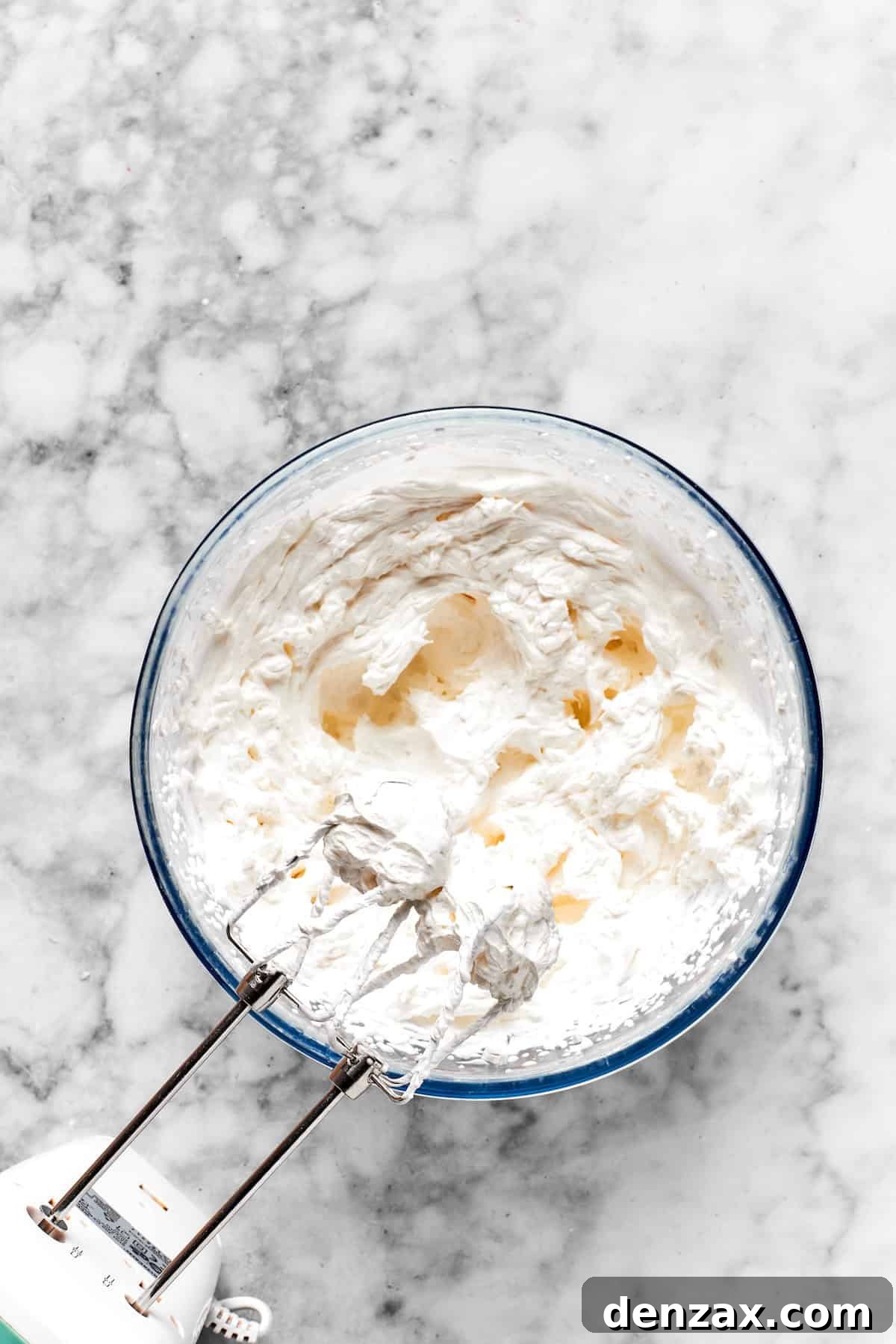 A mixer beats frosting ingredients together in a bowl.
