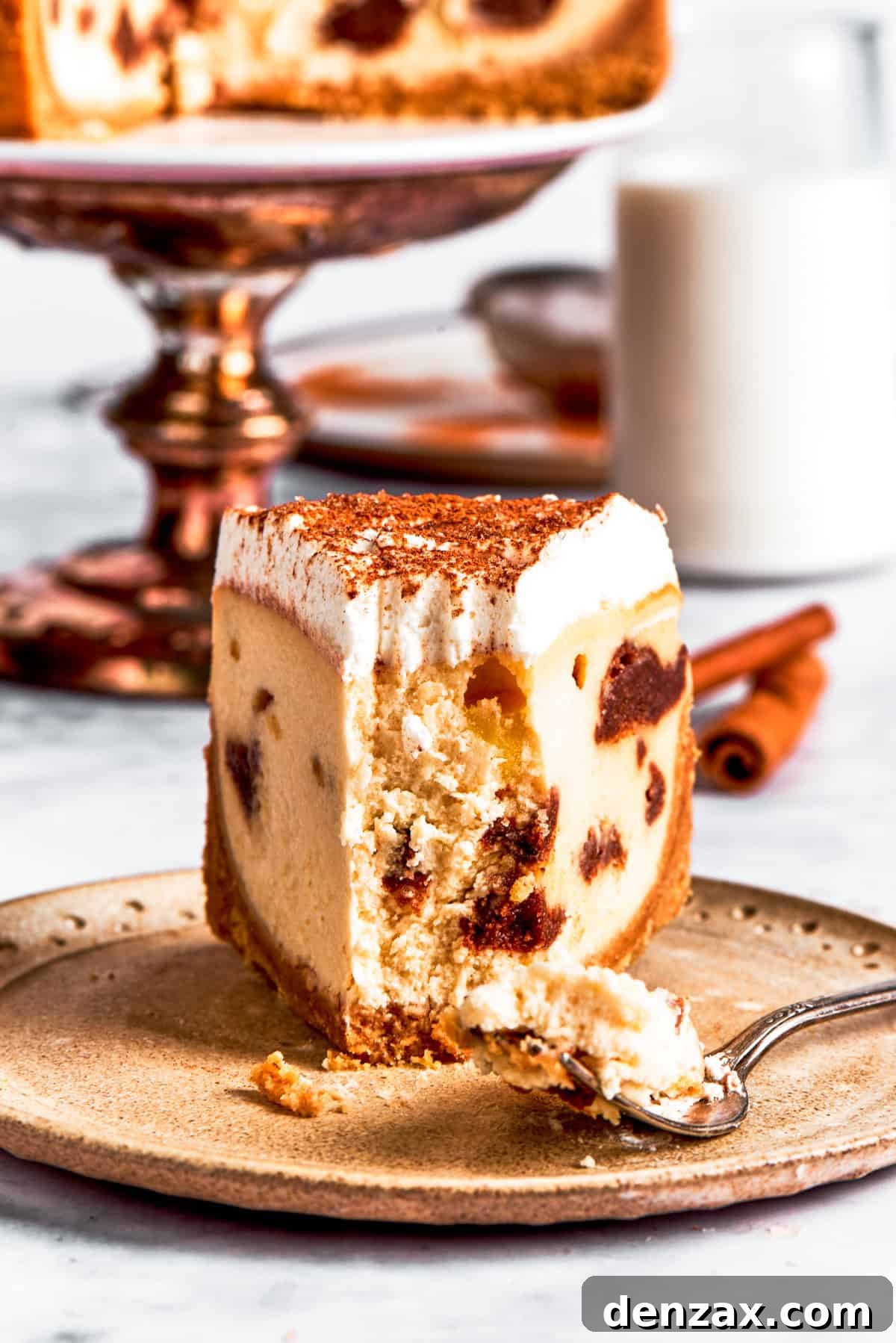 A dessert plate with a slice of cinnamon roll cheesecake with a forkful removed.