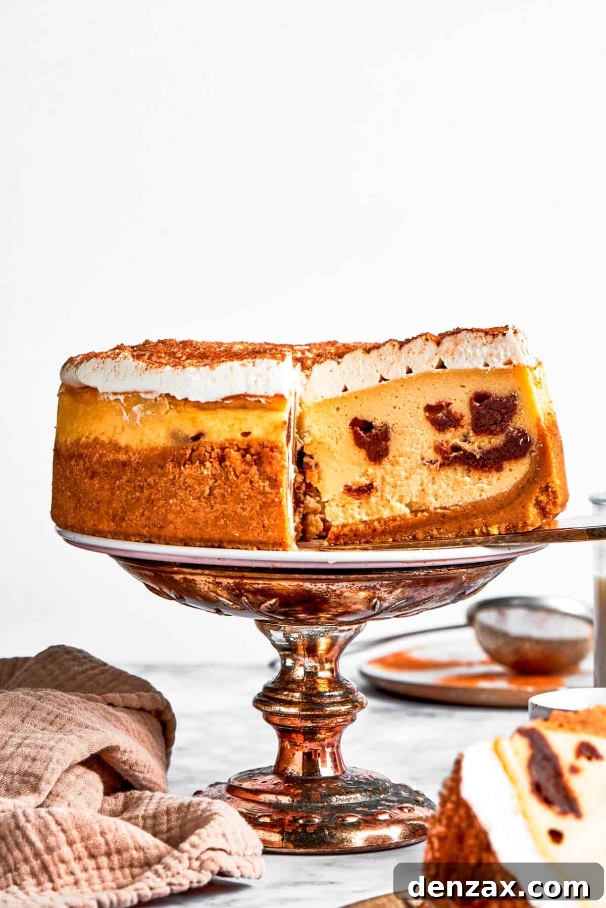 Lifting out a slice of cinnamon roll cheesecake from a whole cheesecake set on a cake platter.